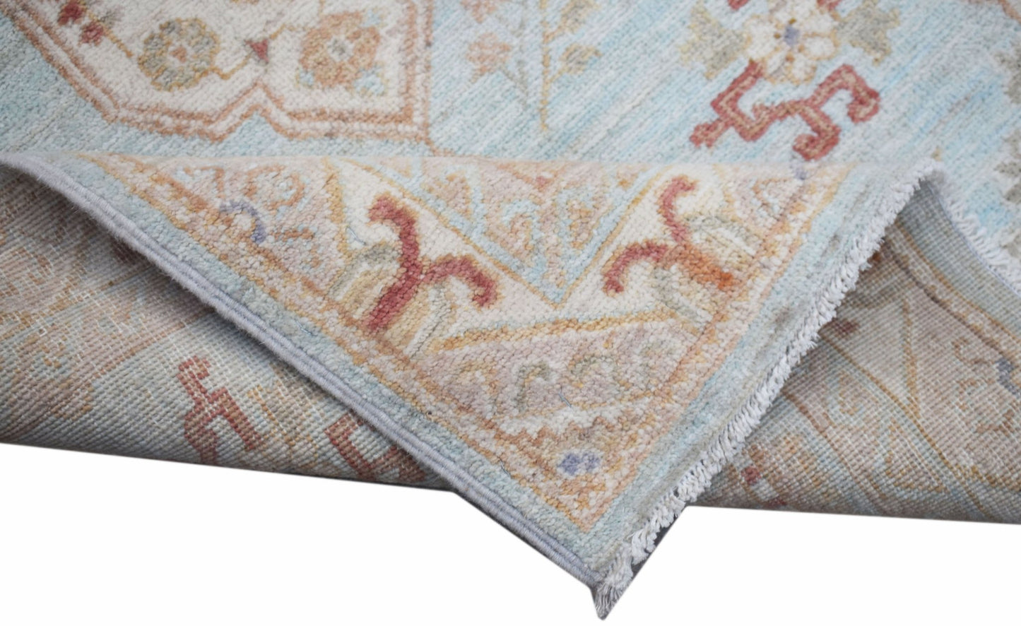 A folded Afghan Chobi rug featuring traditional floral patterns in soft blue and earthy tones.