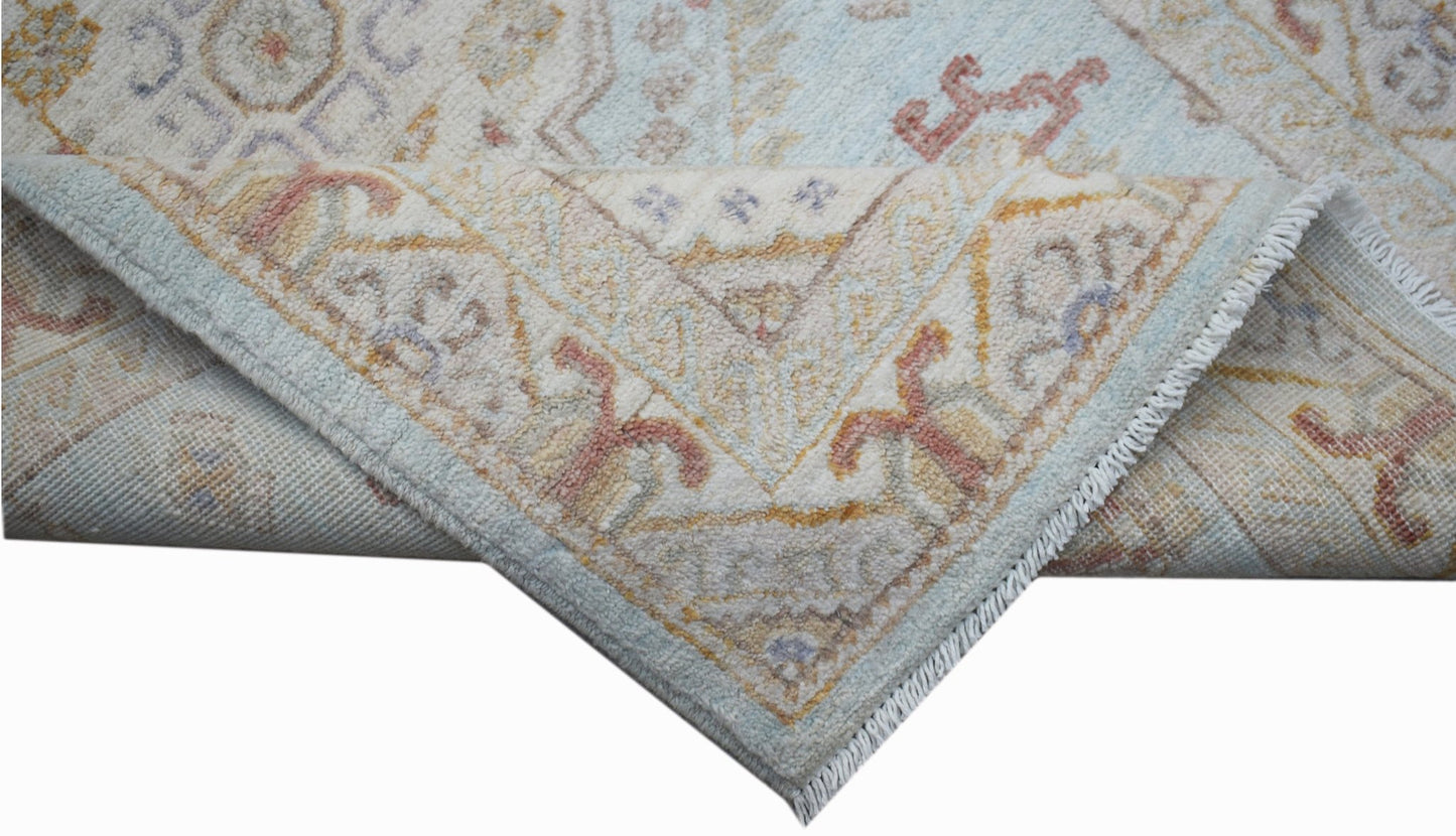 A handwoven Afghan Chobi rug featuring a traditional floral pattern in soft blue and beige tones.