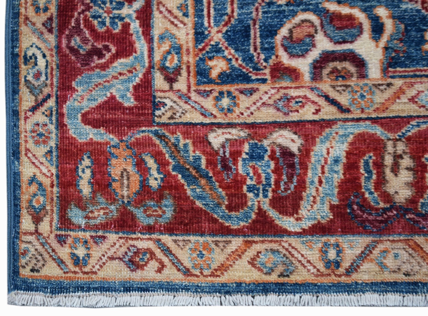 A corner view of a handwoven Afghan Chobi rug featuring intricate floral patterns in red and blue.