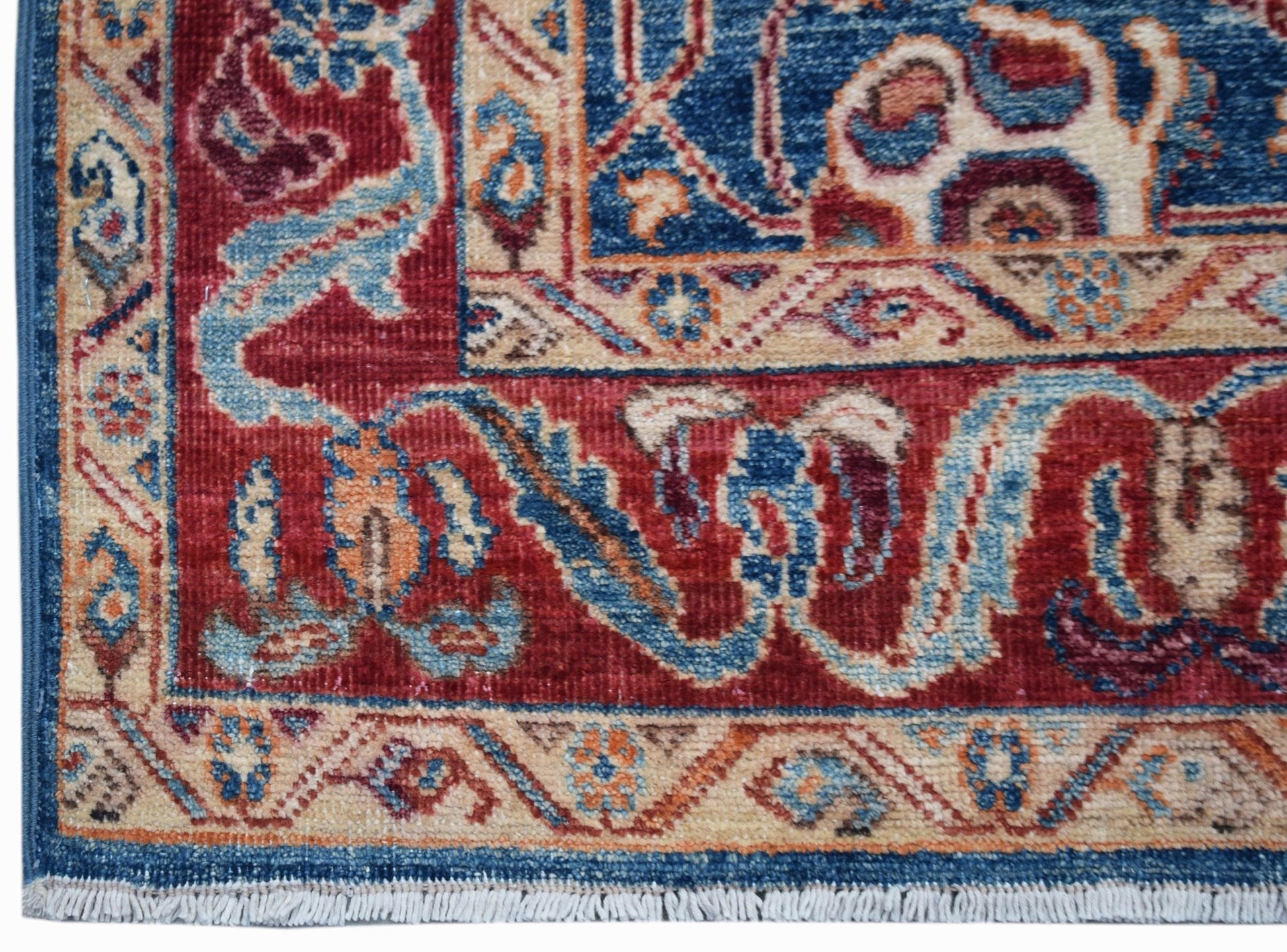 A corner view of a handwoven Afghan Chobi rug featuring intricate floral patterns in red and blue.