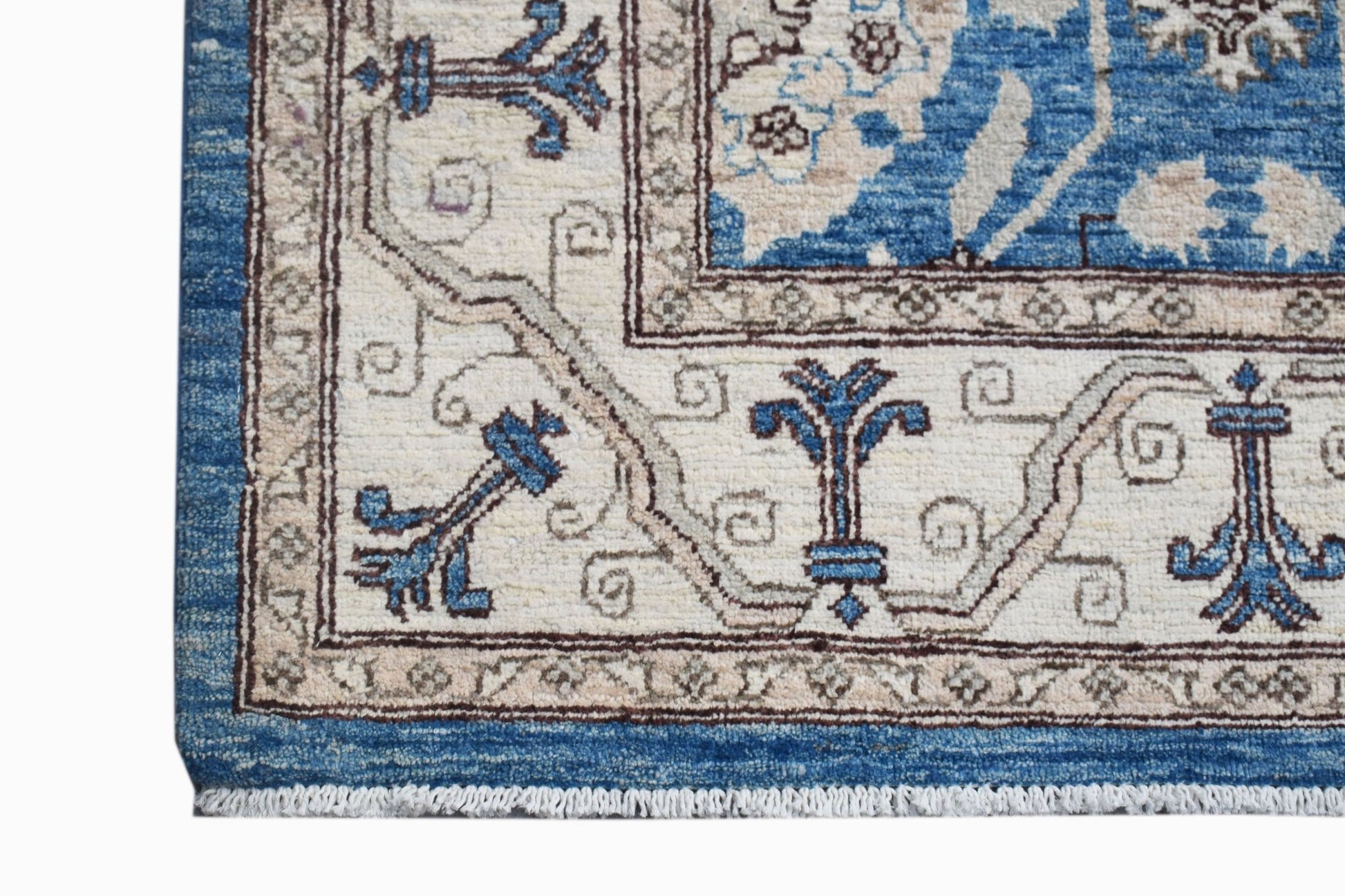 A corner view of a handmade Afghan Chobi rug featuring blue and cream floral patterns.