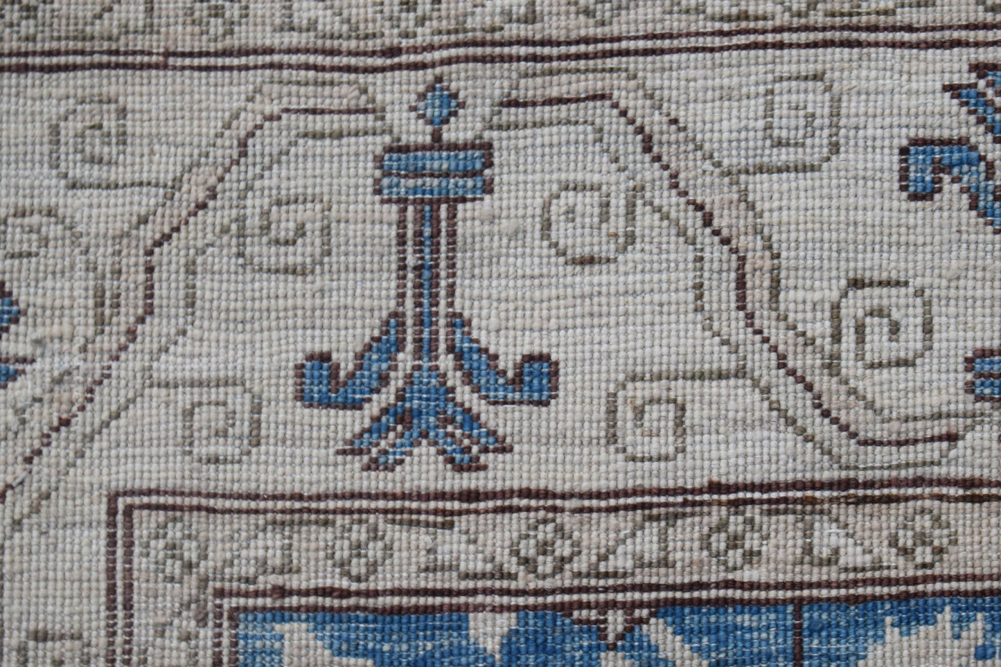 A close-up of a handwoven Afghan Chobi rug featuring a blue floral motif on a cream wool background.