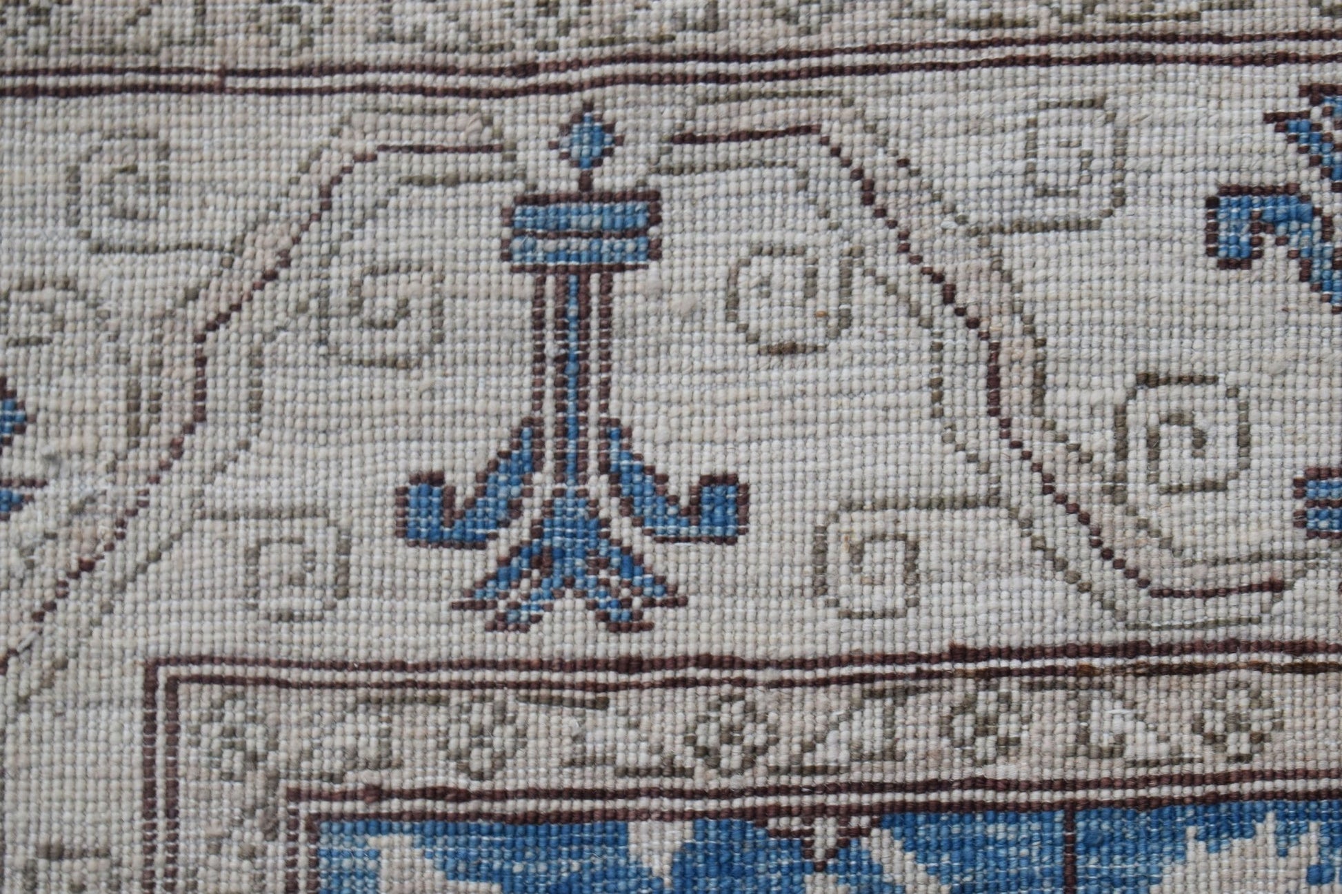 A close-up of a handwoven Afghan Chobi rug featuring a blue floral motif on a cream wool background.