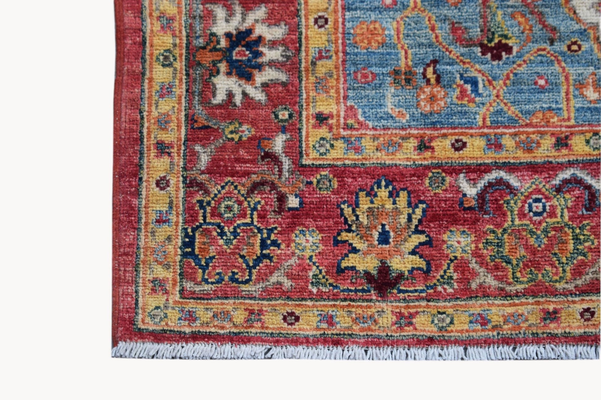 A corner view of a handwoven Afghan Chobi rug featuring traditional floral patterns in red and blue.