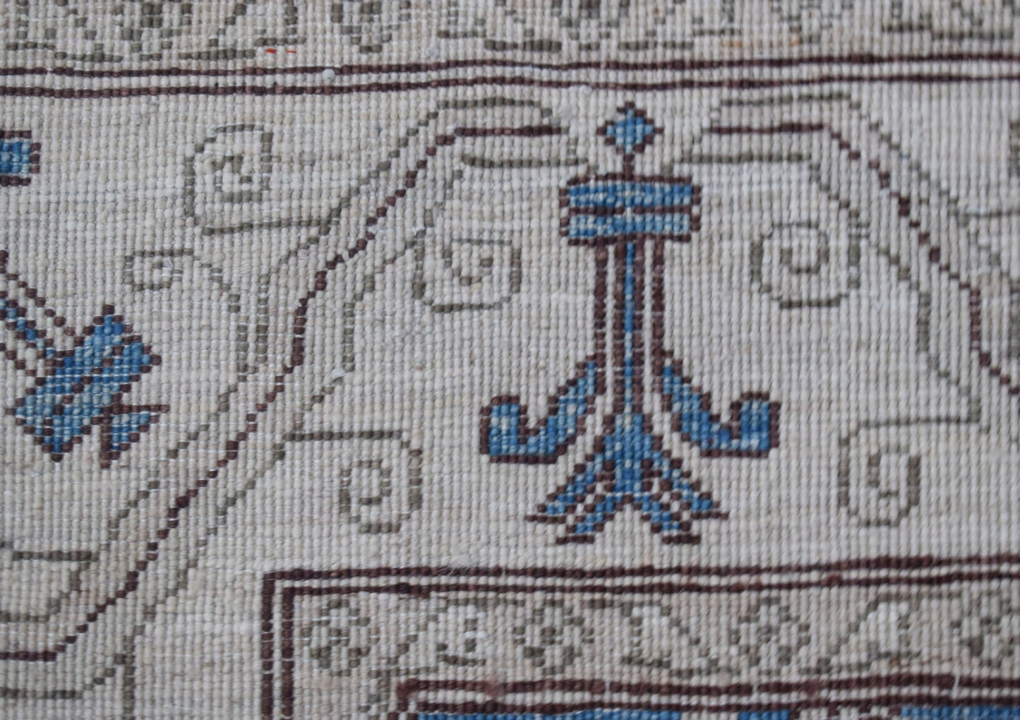 A close-up of an Afghan Chobi rug featuring intricate blue and brown floral motifs on a cream base.