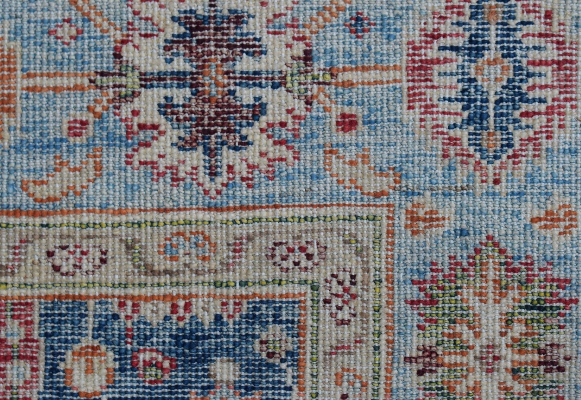 A close-up of a handwoven Afghan Chobi rug featuring intricate geometric patterns in blue and red.