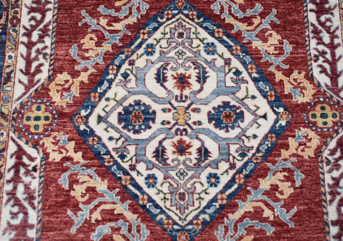 A handmade Afghan Chobi rug featuring a central diamond medallion in blue, red, and cream tones.
