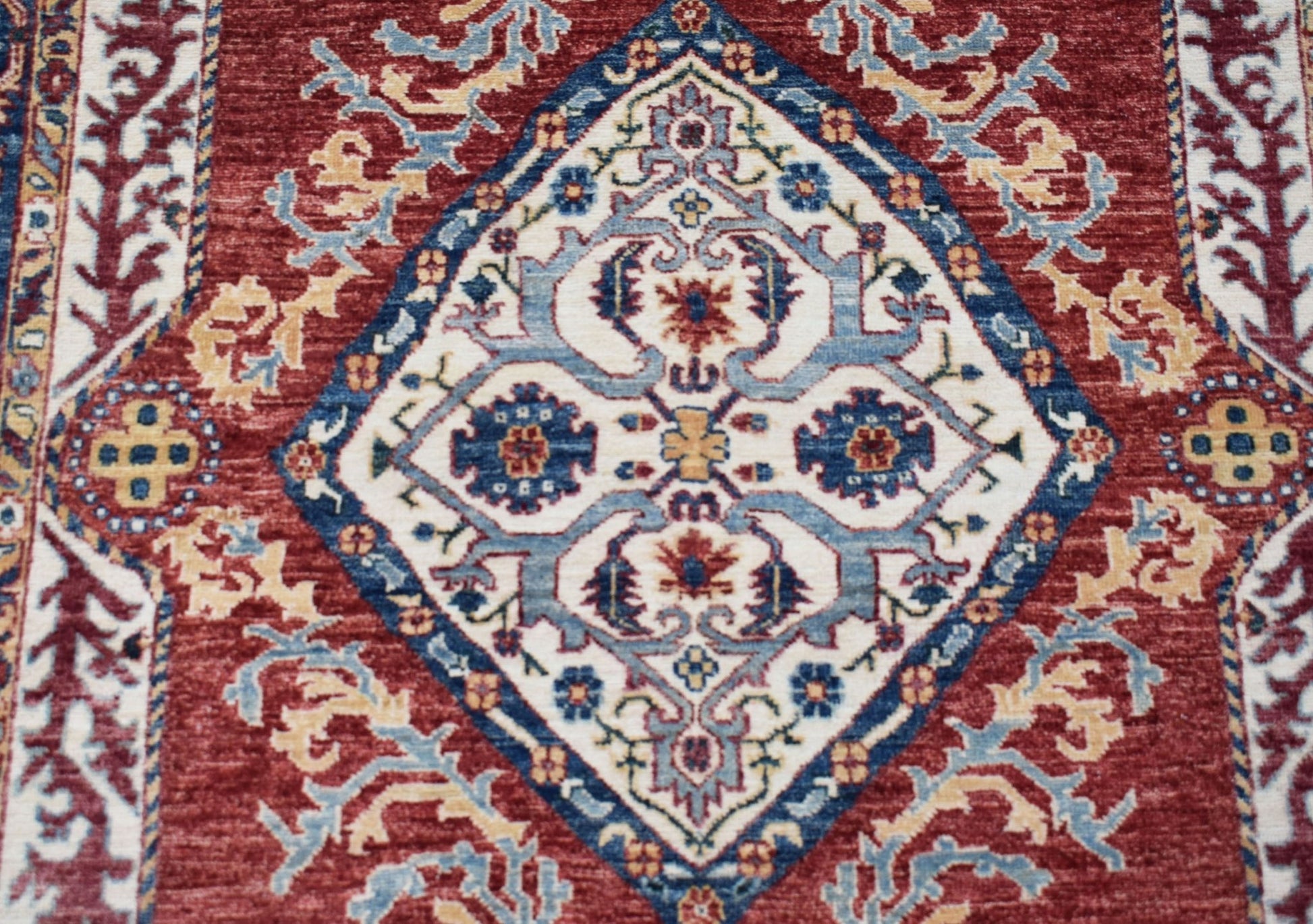 A handmade Afghan Chobi rug featuring a central diamond medallion in blue, red, and cream tones.