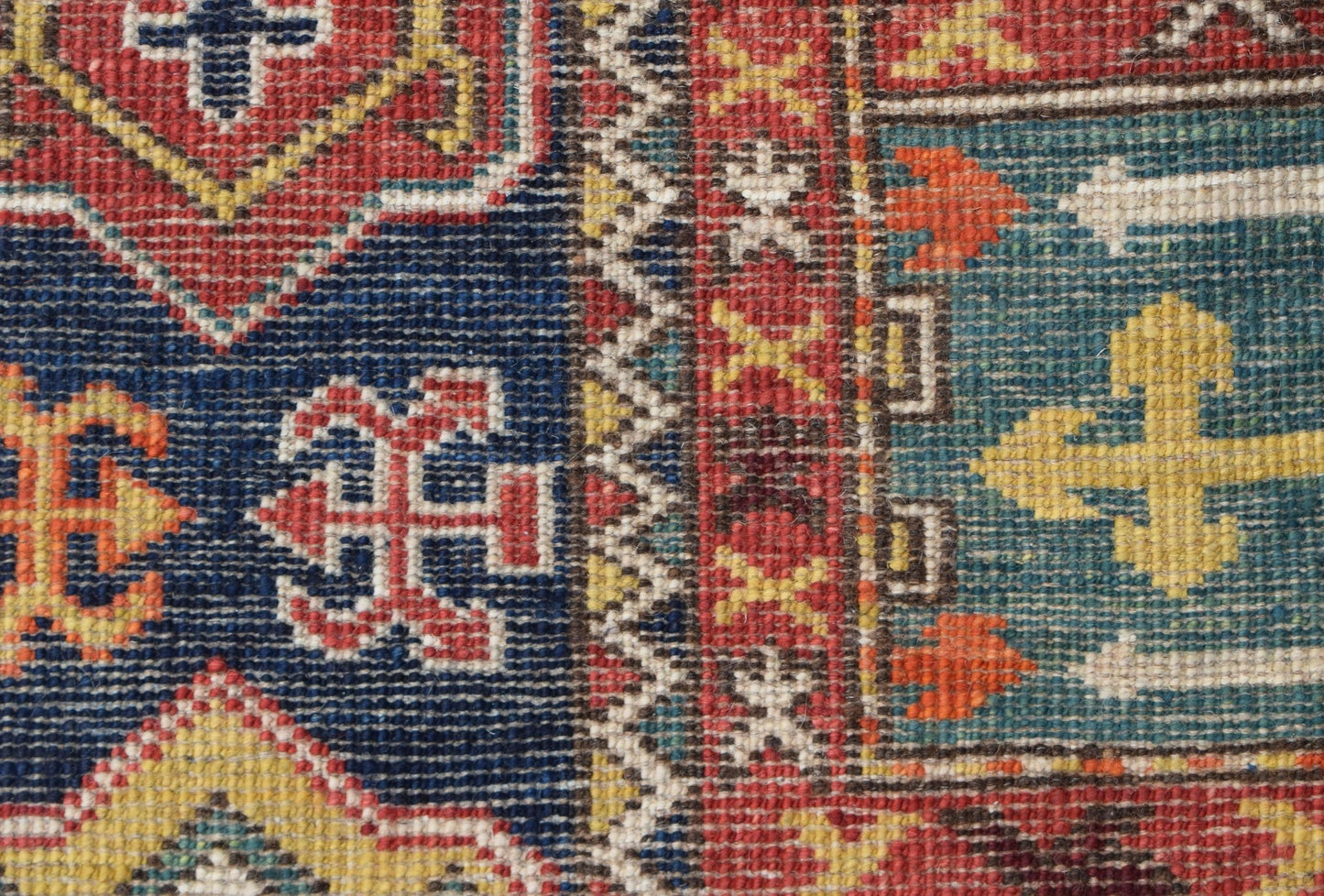 A close-up of a handwoven Afghan Chobi rug featuring geometric patterns in blue, red, and yellow.