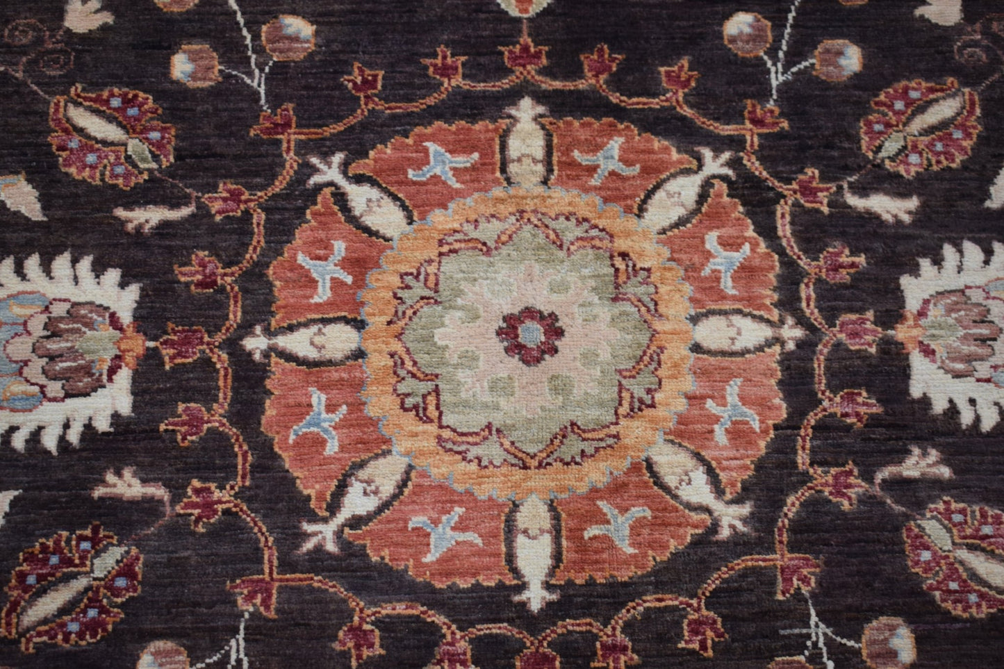 A handmade Afghan Chobi rug featuring a central floral medallion in orange and green on dark brown.