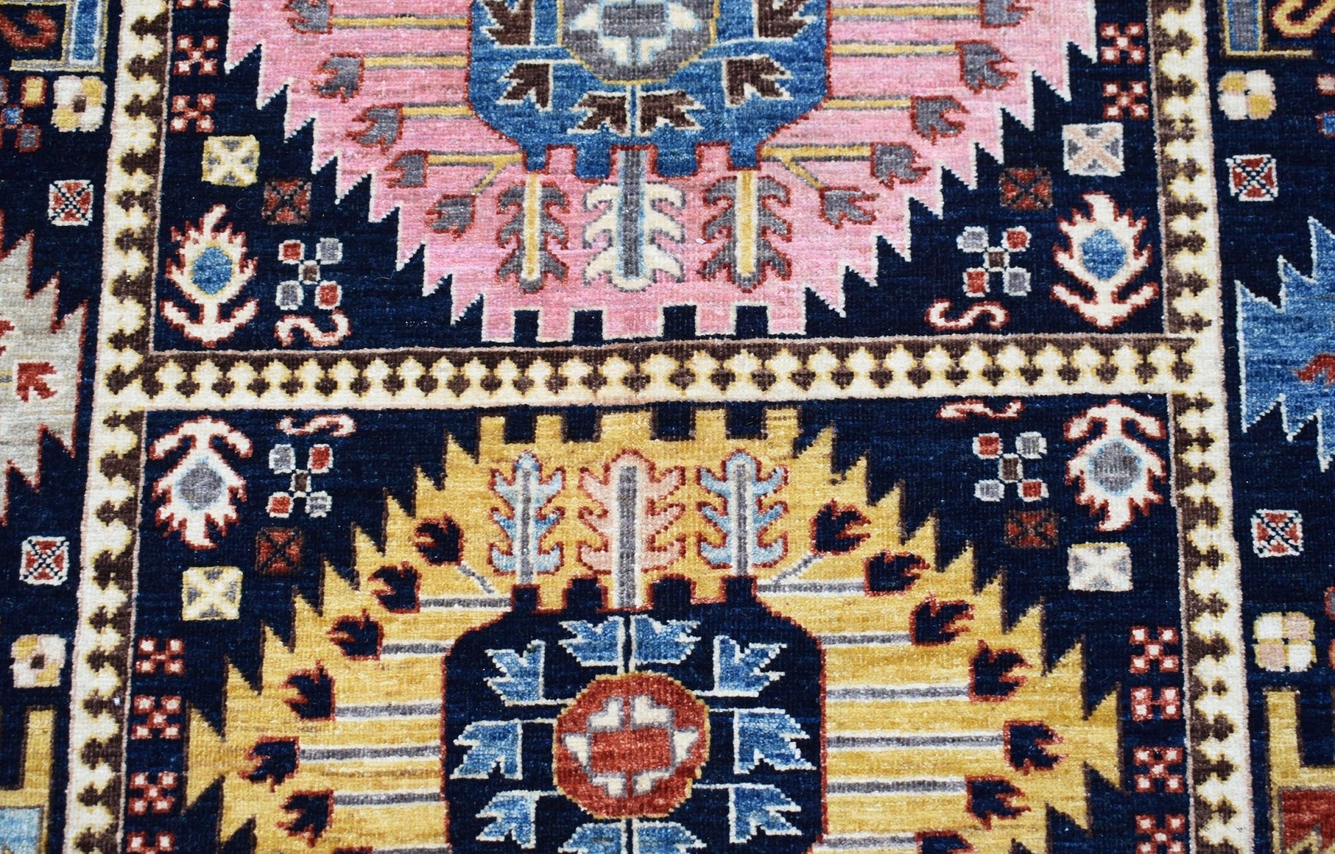 A handwoven Afghan Chobi rug featuring geometric floral medallions in pink, yellow, and blue.