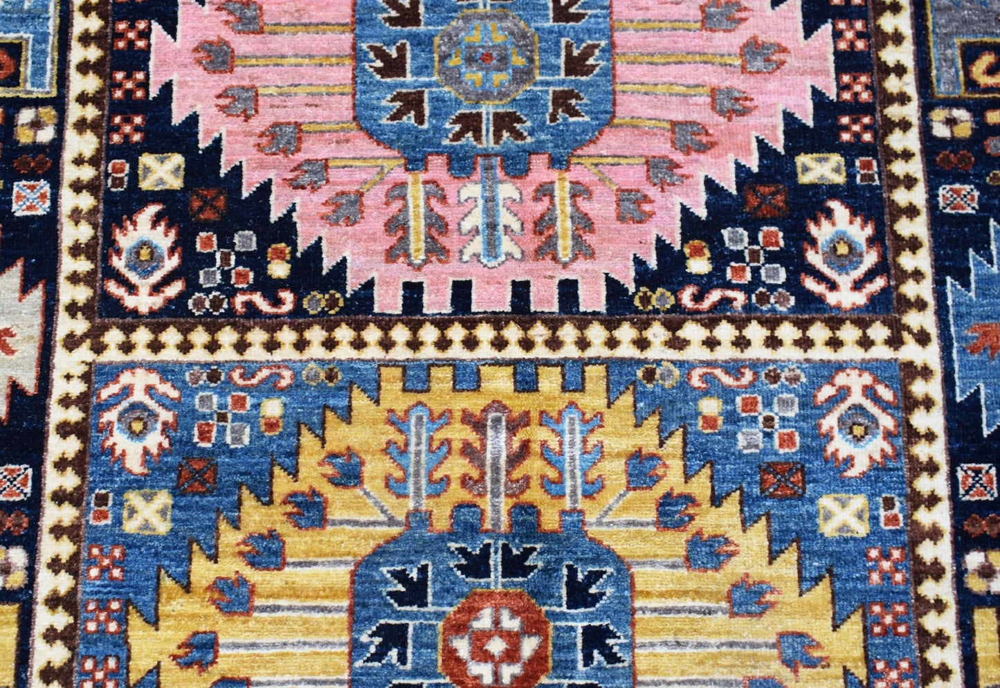 A handwoven Afghan Chobi rug featuring geometric patterns in blue, pink, and yellow wool.