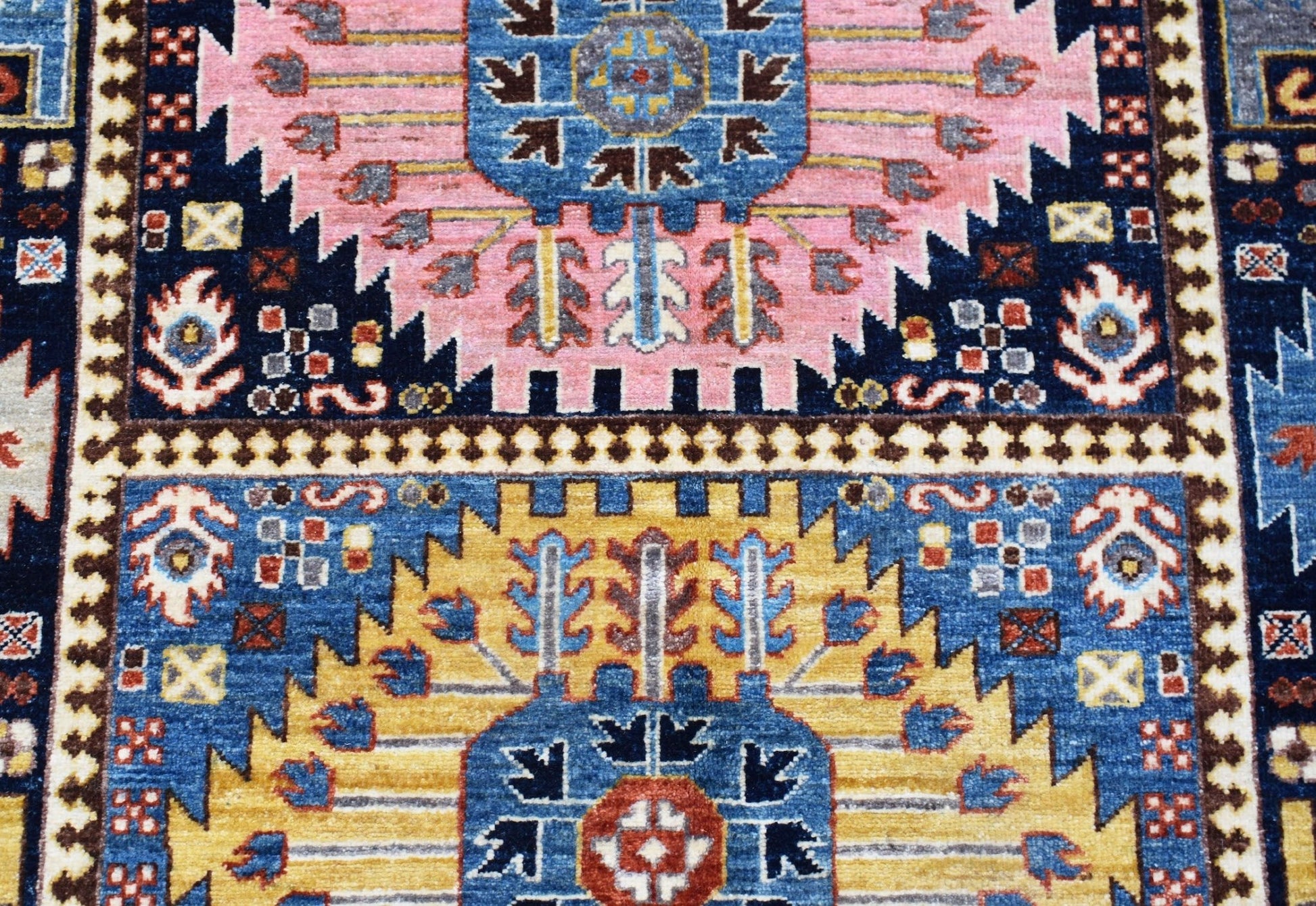 A handwoven Afghan Chobi rug featuring geometric patterns in blue, pink, and yellow wool.