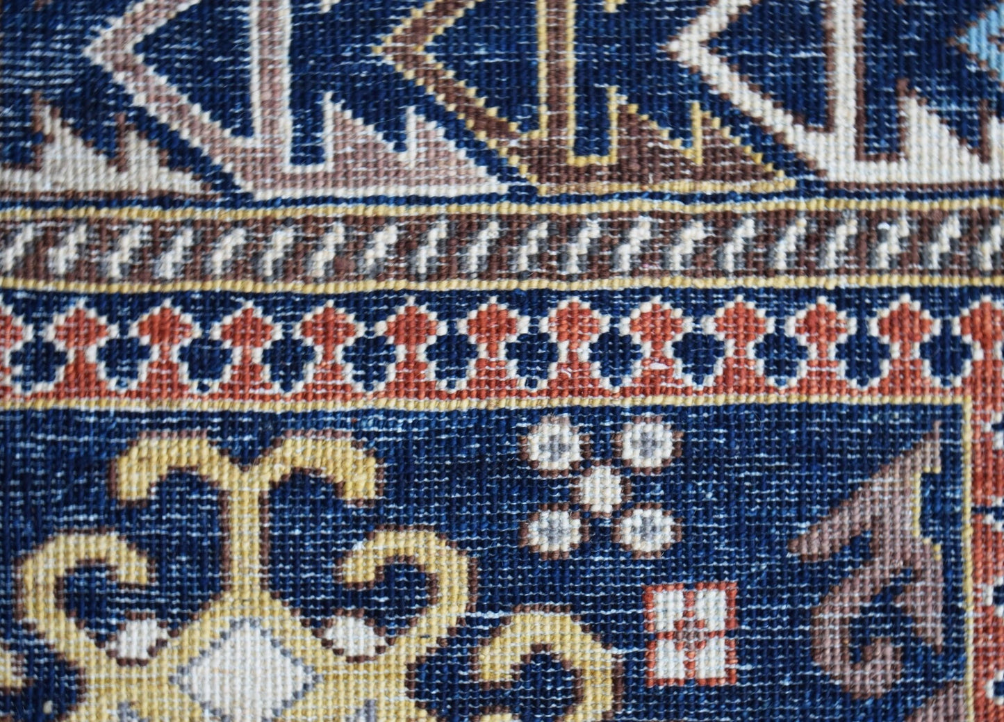 A close-up view of a handwoven Afghan Chobi rug featuring intricate geometric patterns in blue, gold, and rust tones.