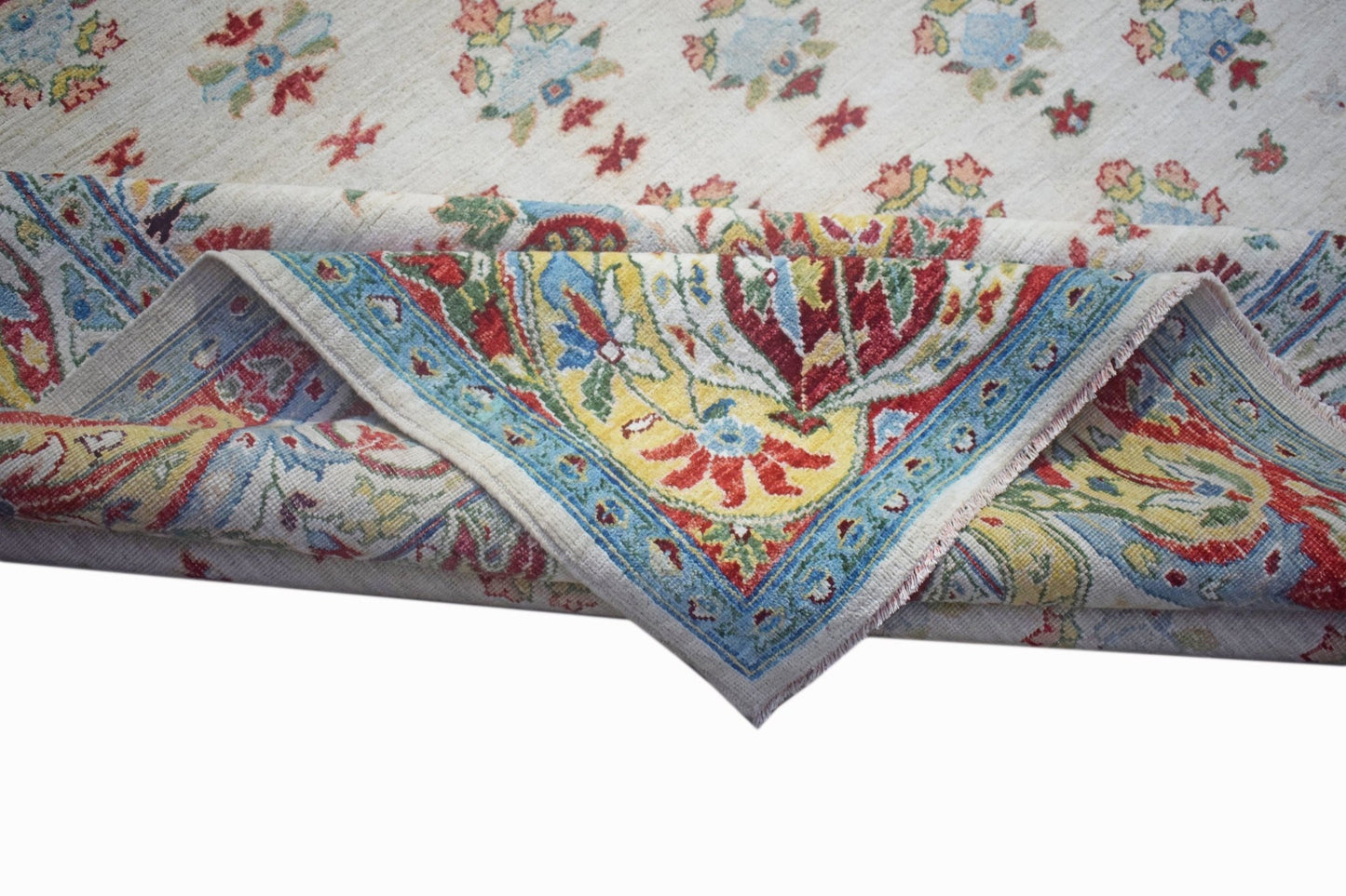 A handwoven Afghan Chobi rug with a cream field and a vibrant floral border folded over.