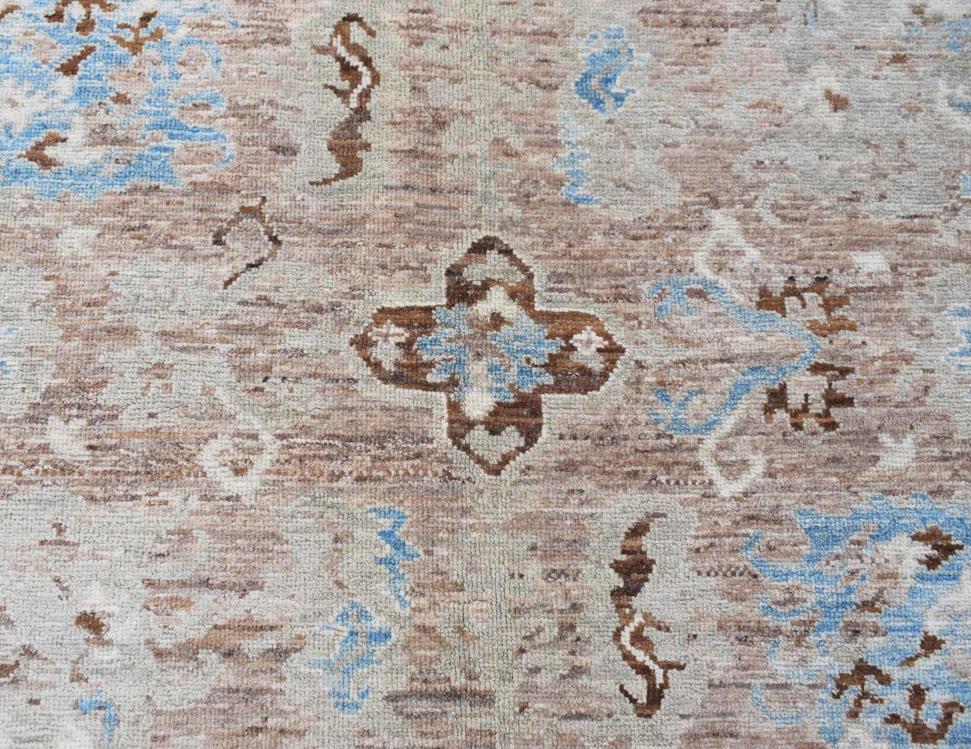 A transitional Oushak rug featuring a brown and blue geometric floral pattern on a wool pile.