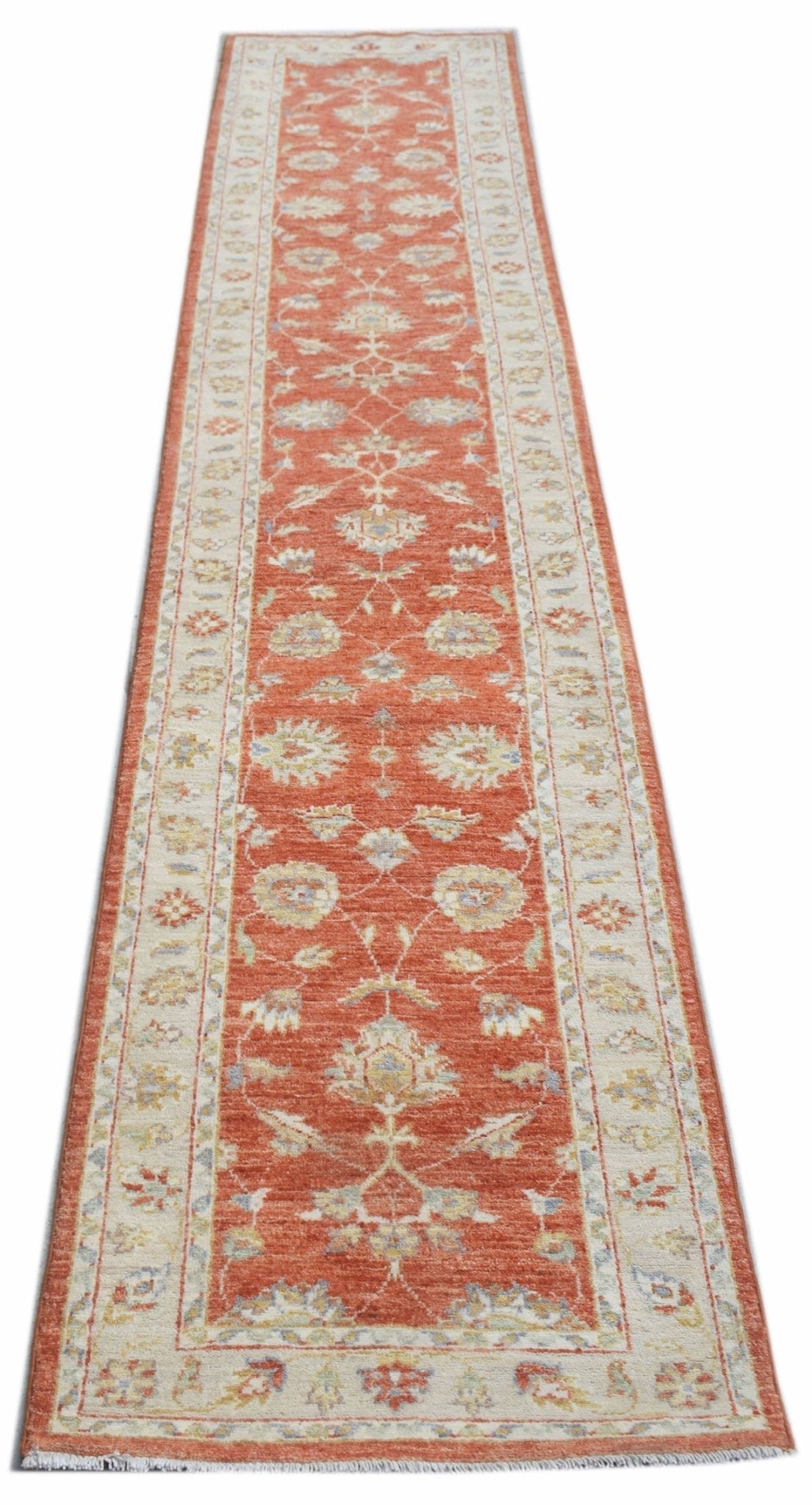 A handmade Afghan Chobi runner rug featuring a traditional floral pattern in terracotta and cream.