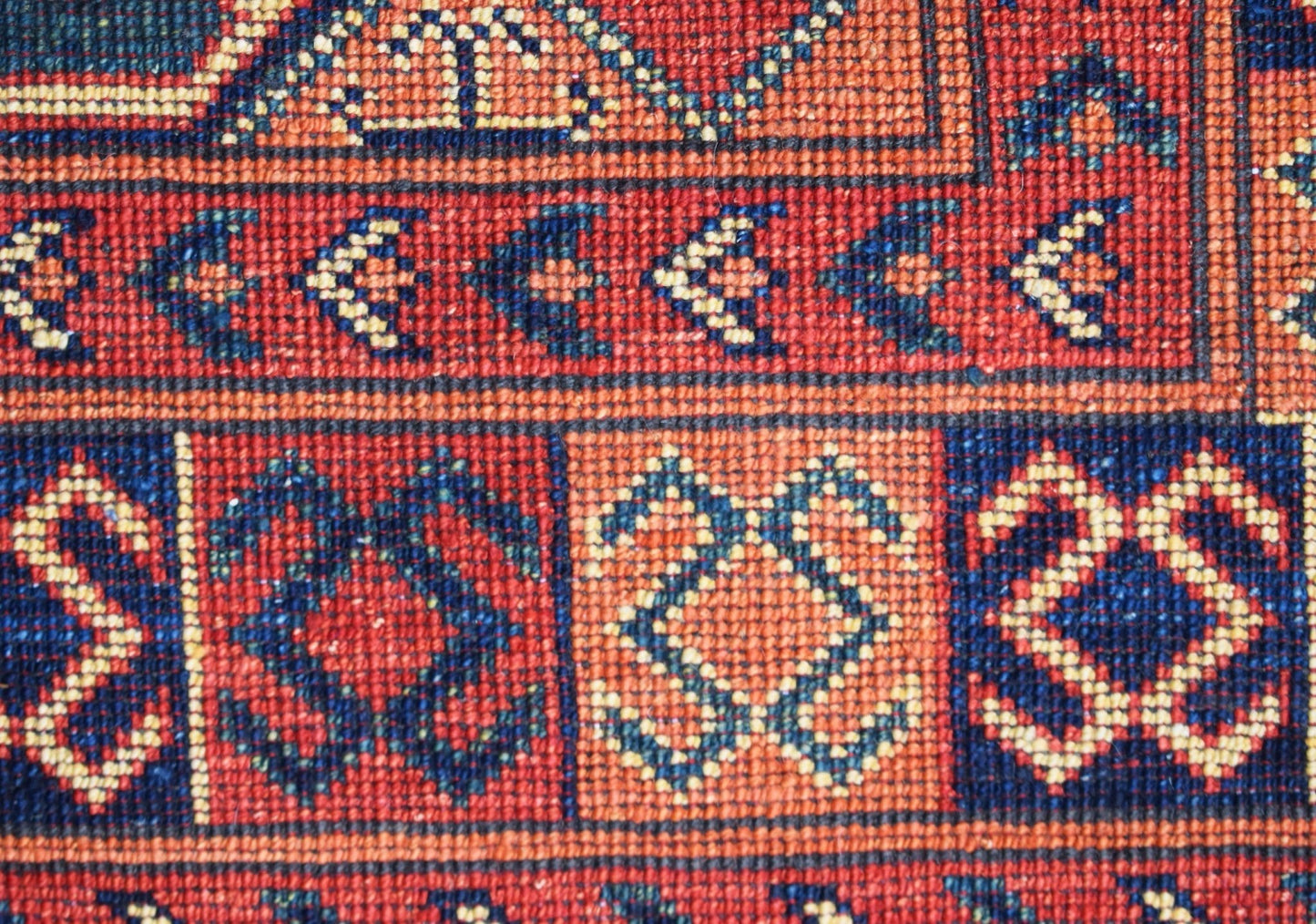 A close-up of a handwoven Afghan Chobi runner featuring geometric patterns in red and blue wool.