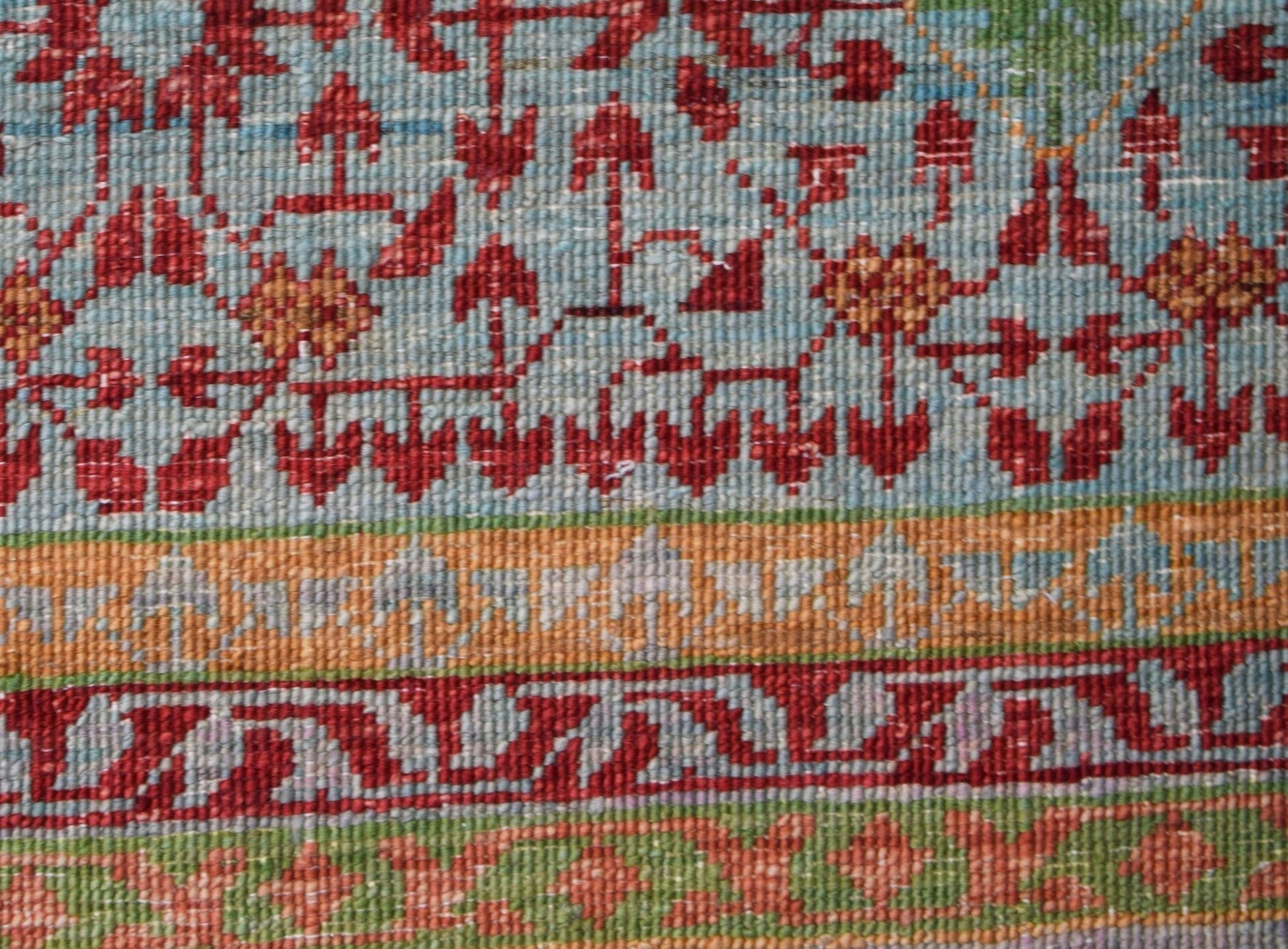 A close-up of an Afghan Chobi rug featuring intricate red floral patterns on a light blue field.