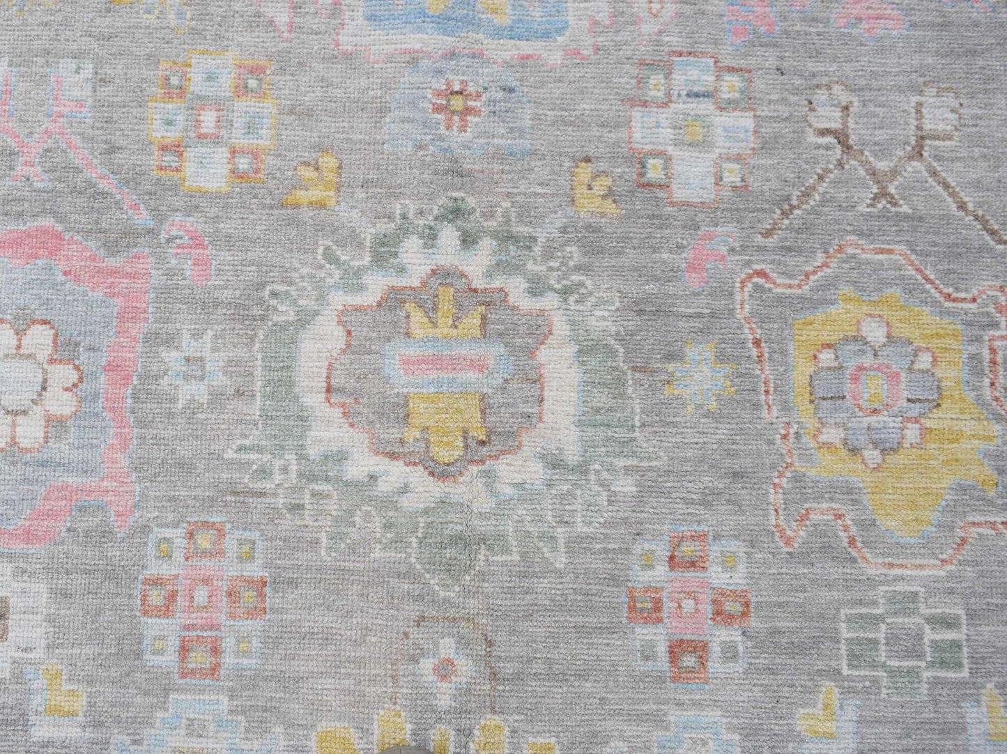 A transitional Oushak rug featuring a floral pattern in soft pastel tones on a grey wool background.