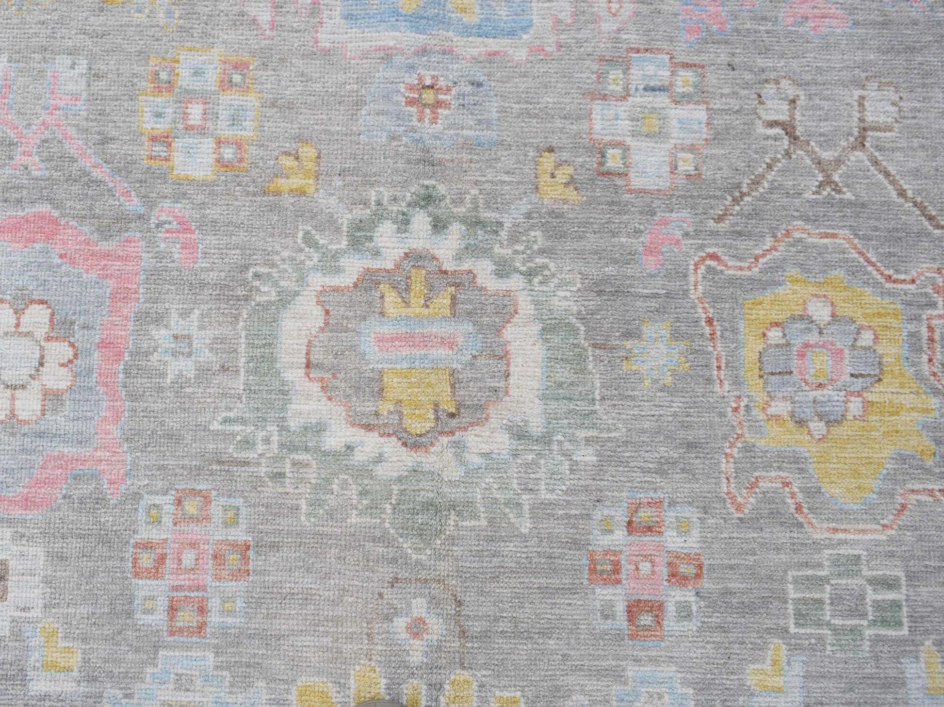 A transitional Oushak rug featuring a floral pattern in soft pastel tones on a grey wool background.