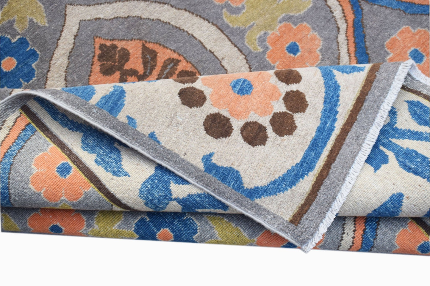 A folded Afghan Chobi rug featuring a traditional floral pattern in blue, orange, and grey tones.