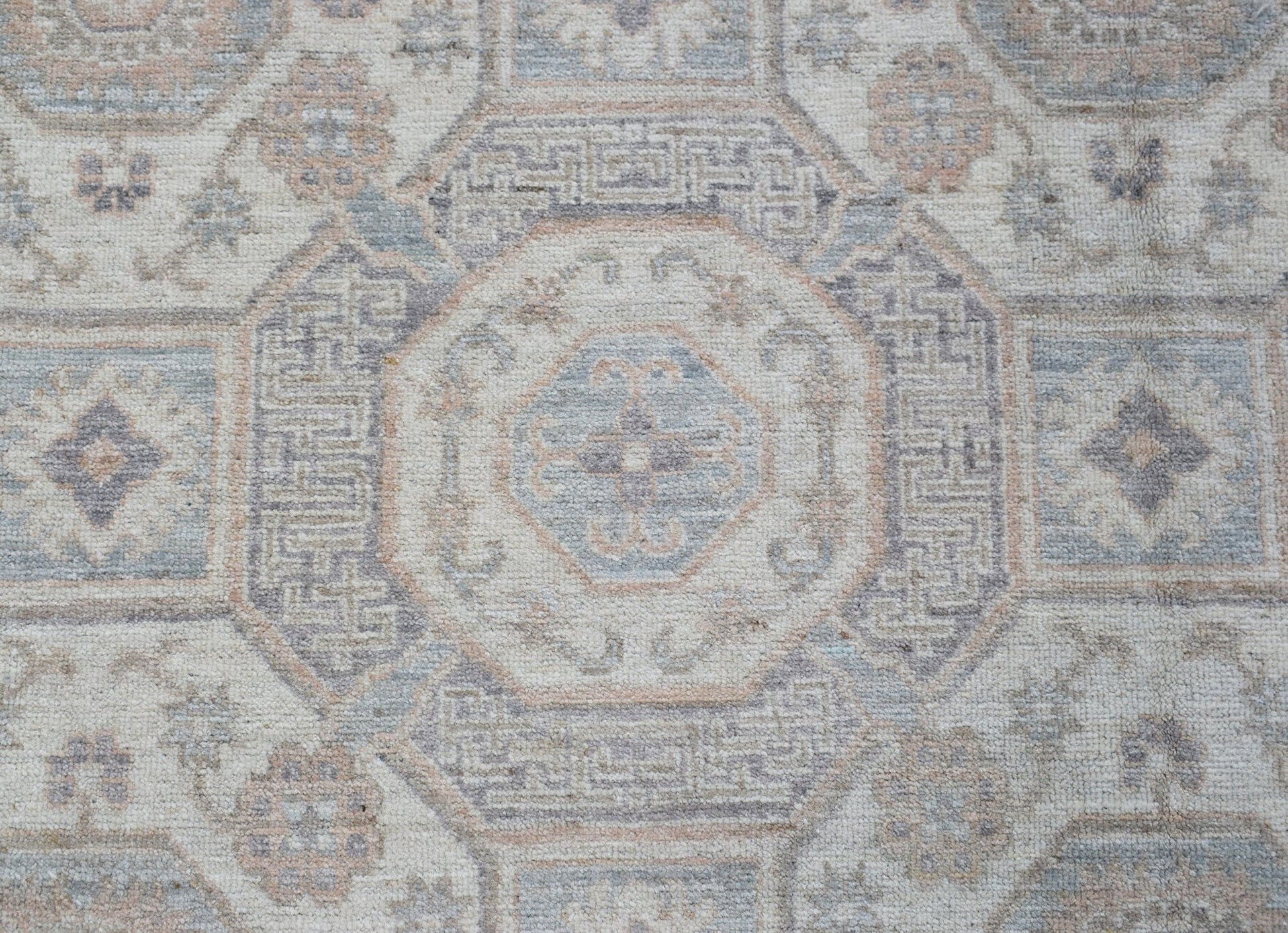 A handmade Afghan Chobi rug featuring a traditional geometric pattern in soft blue and beige tones.