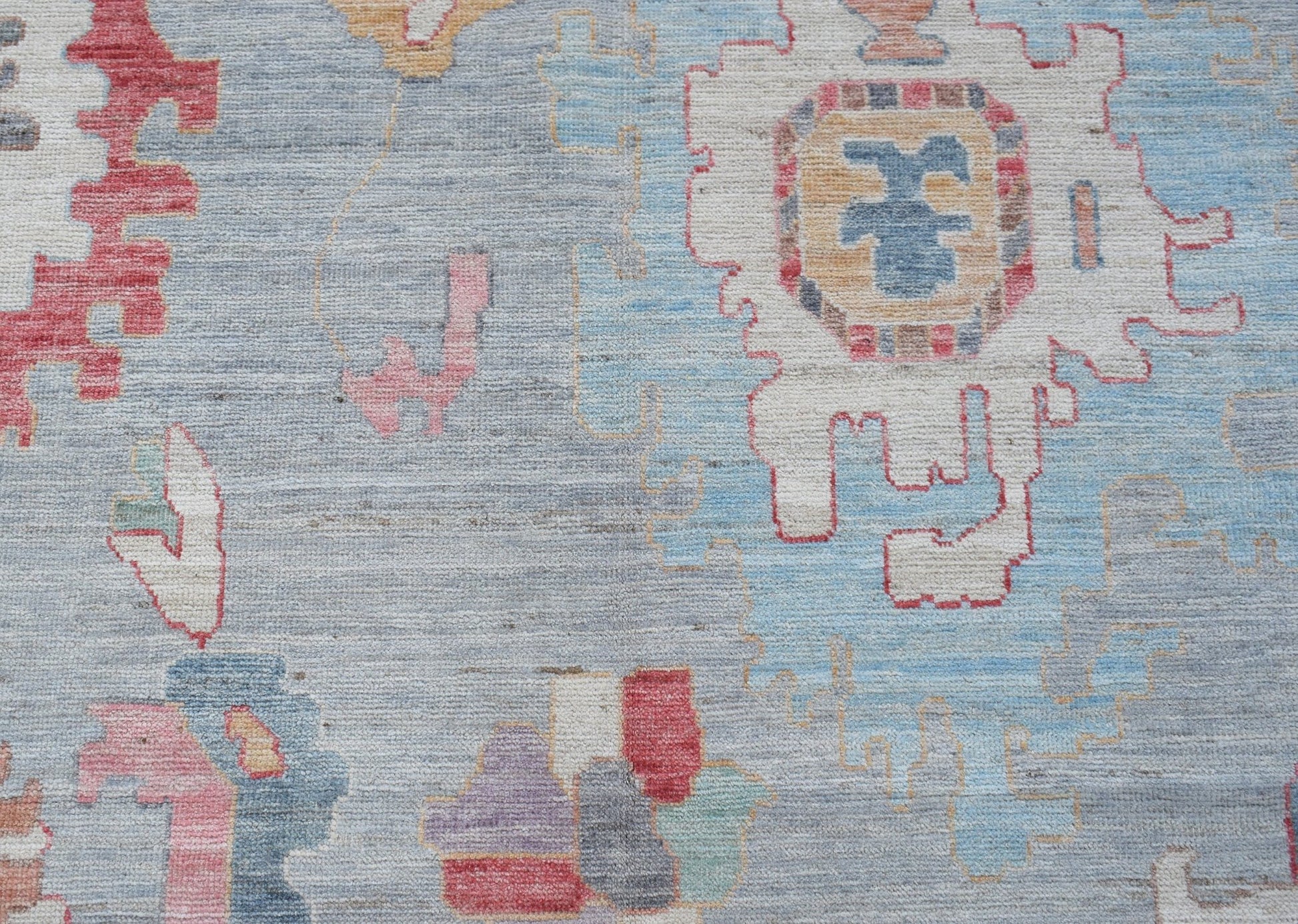 A transitional Oushak rug featuring geometric pomegranate motifs in a soft blue and multi-color palette.