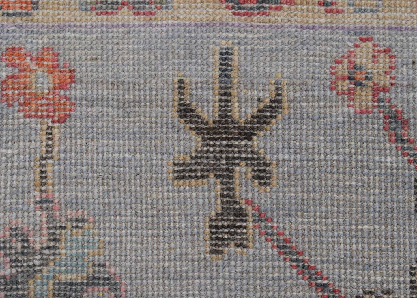 A handwoven wool runner featuring a stylized dark floral motif on a light blue background.