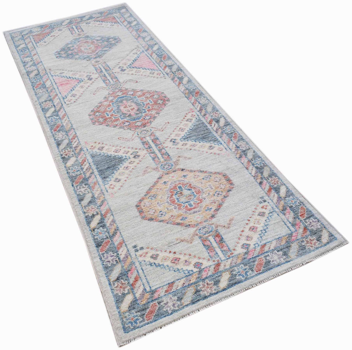 A handwoven wool runner rug featuring a transitional Oushak pattern in blue, pink, and cream tones.
