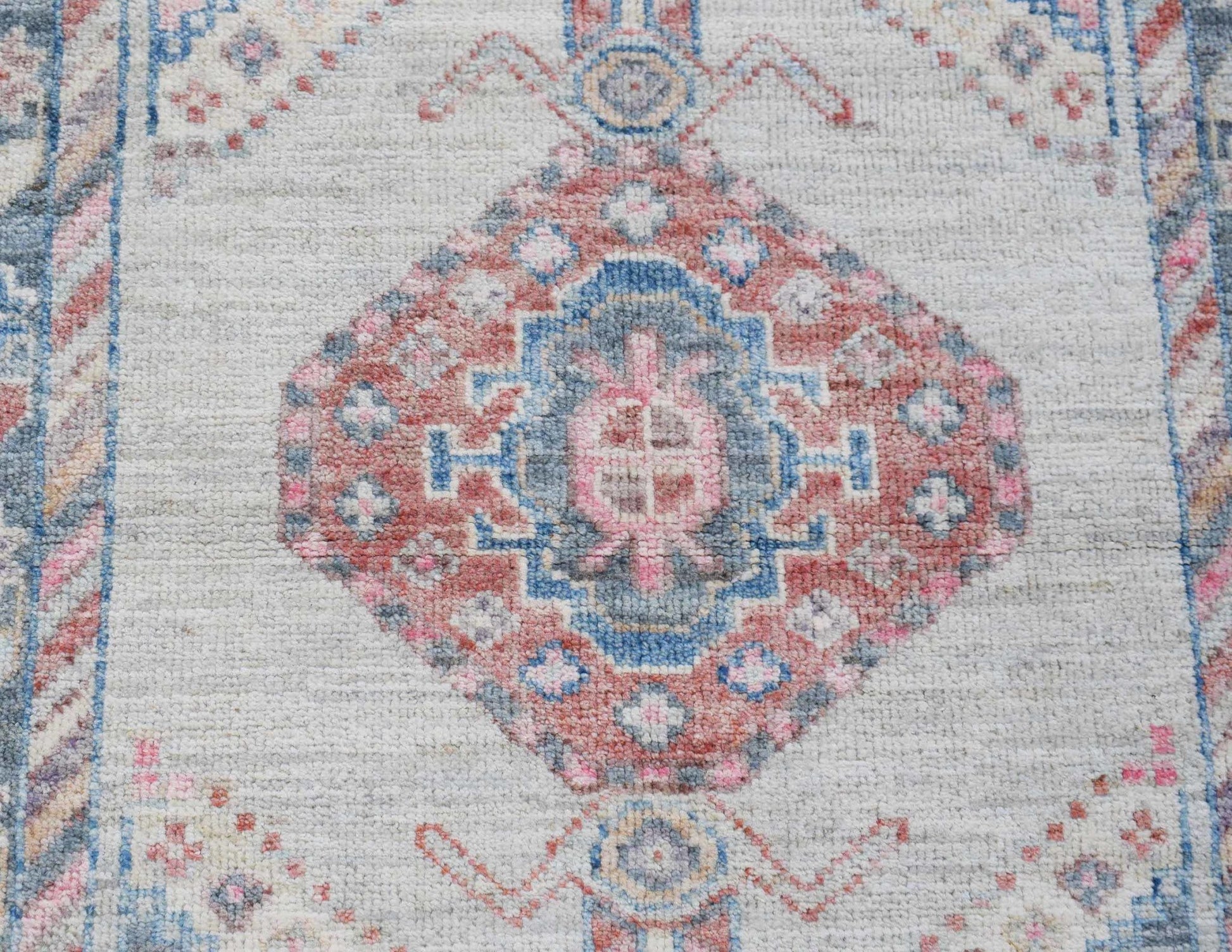 A handwoven wool runner rug featuring a central floral medallion in muted pink and blue tones.