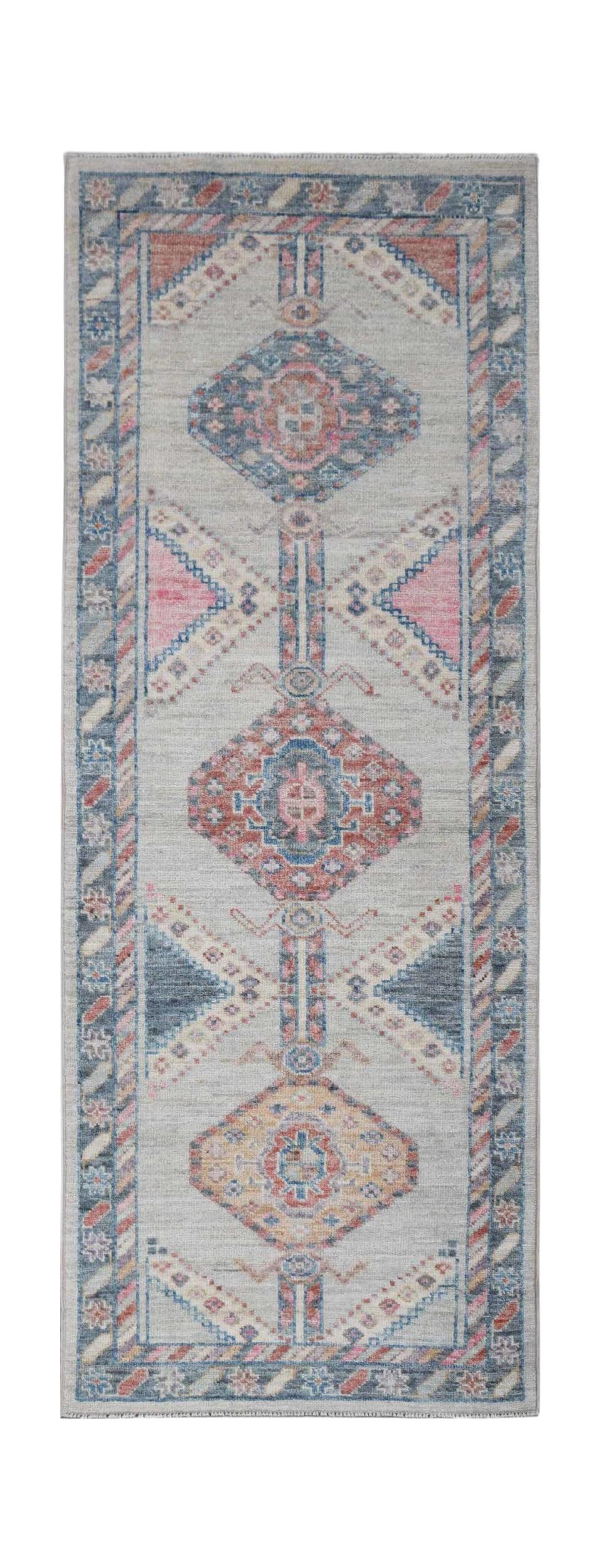A handwoven wool runner rug featuring a transitional Oushak pattern in blue, pink, and grey tones.