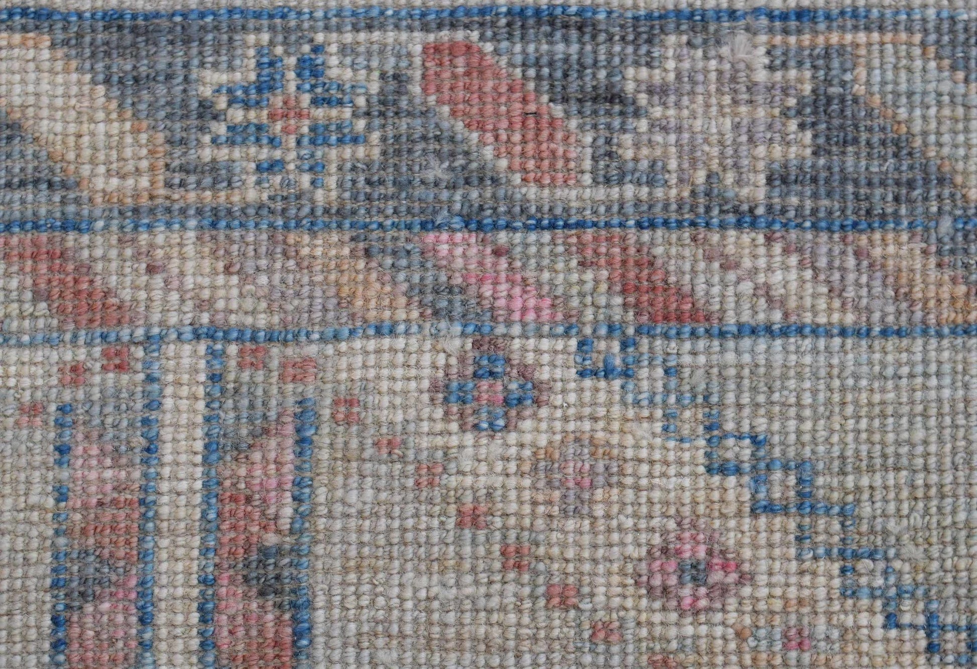 A close-up of a handwoven wool runner rug featuring a transitional floral pattern in muted tones.
