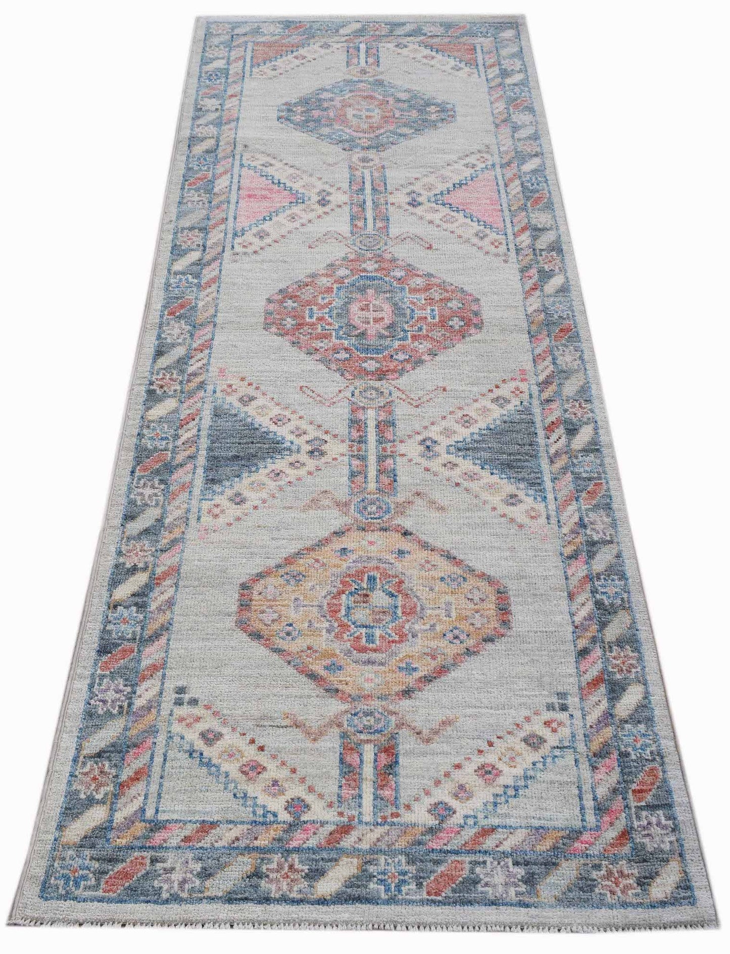 A handwoven wool runner rug featuring a transitional Oushak pattern in blue, pink, and cream tones.