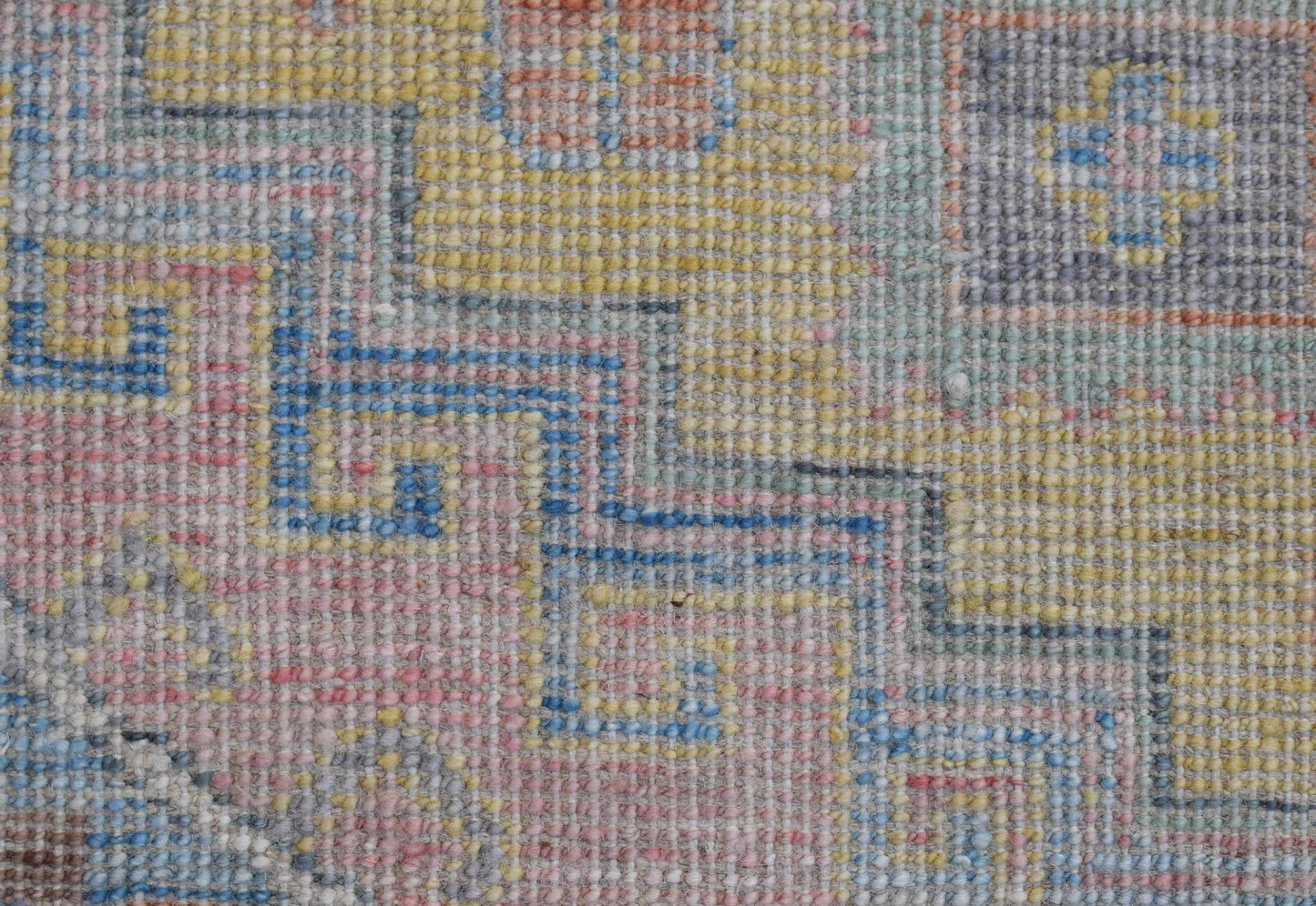 A close-up of a handwoven wool runner featuring a geometric pattern in soft, muted colors.