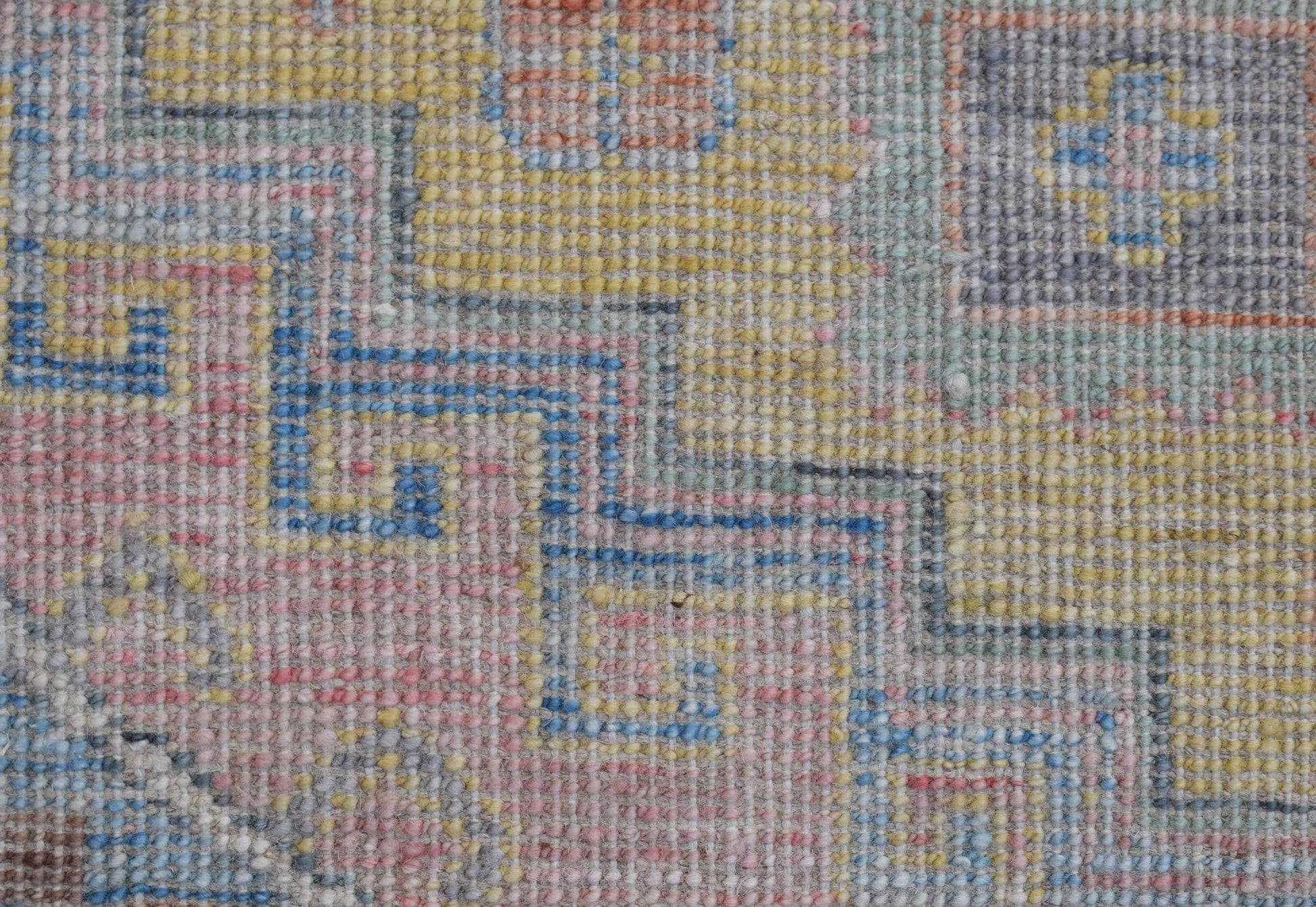 A close-up of a handwoven wool runner featuring a geometric pattern in soft, muted colors.