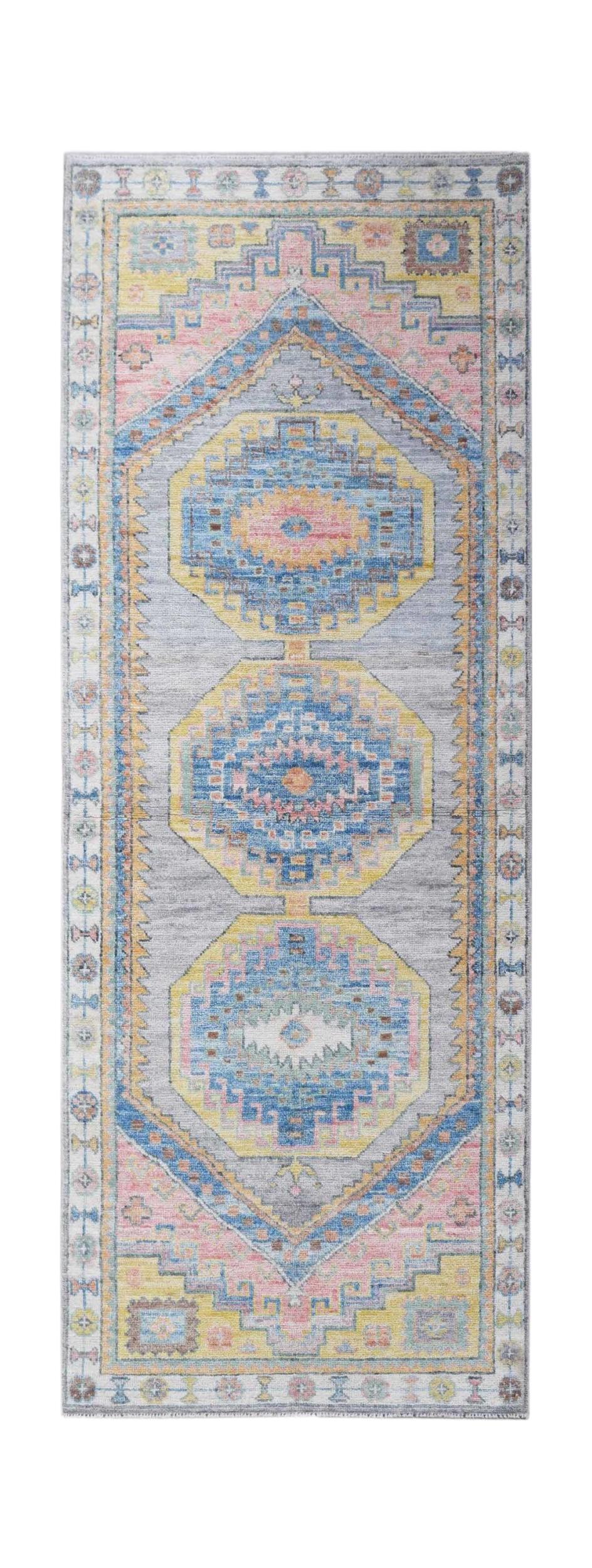 A handwoven wool runner rug featuring a transitional Oushak pattern in blue, pink, and yellow.