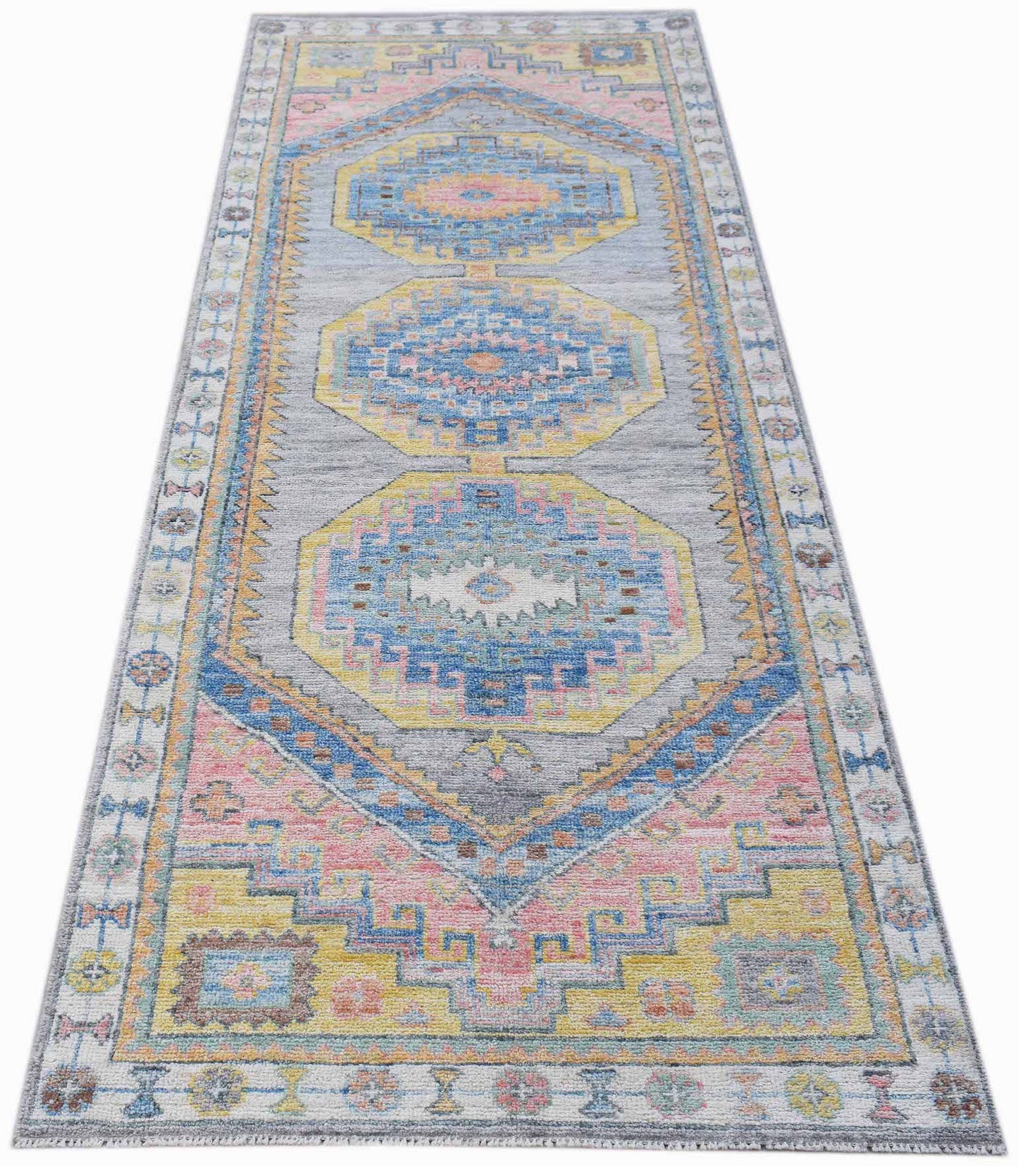 A handwoven wool runner rug featuring a transitional Oushak pattern in blue, pink, and yellow.