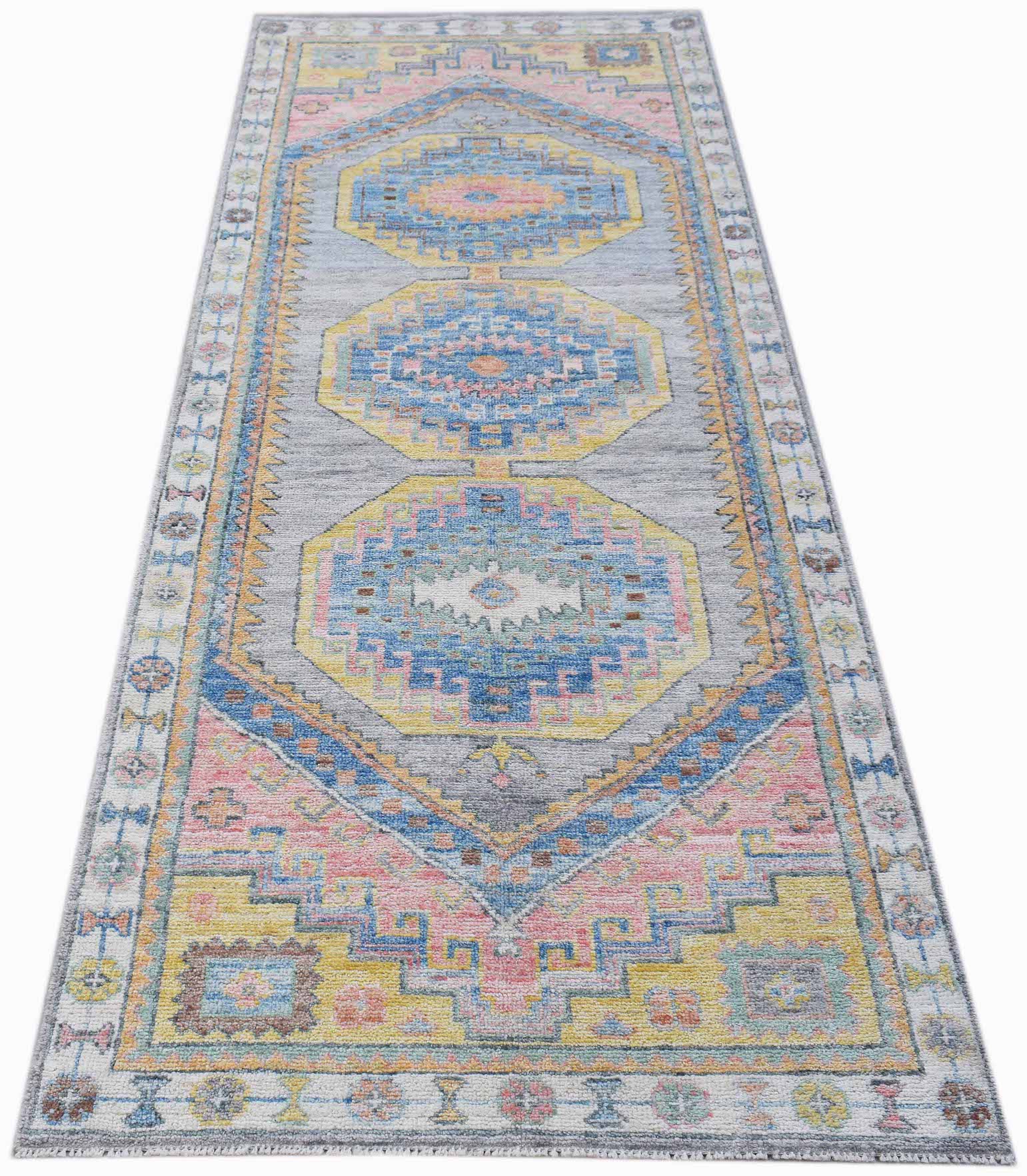 A handwoven wool runner rug featuring a transitional Oushak pattern in blue, pink, and yellow.