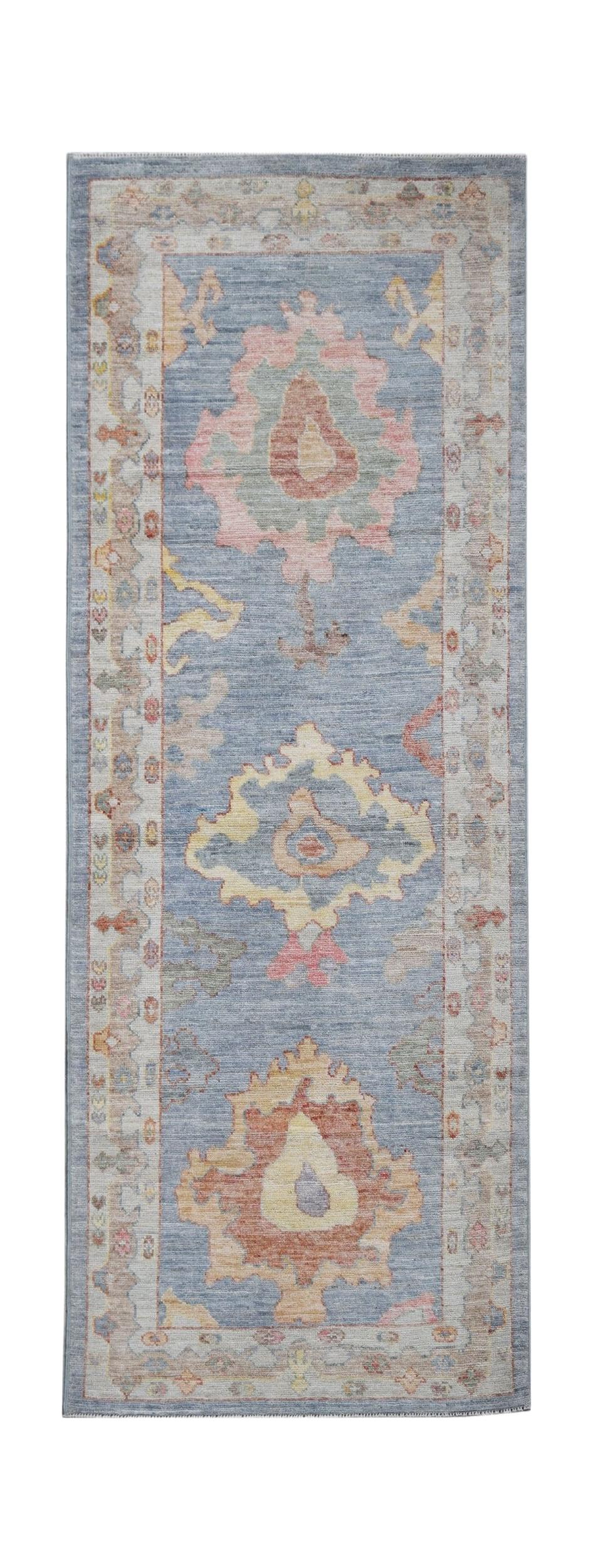 A handwoven wool runner rug featuring a blue field with traditional floral motifs in soft colors.