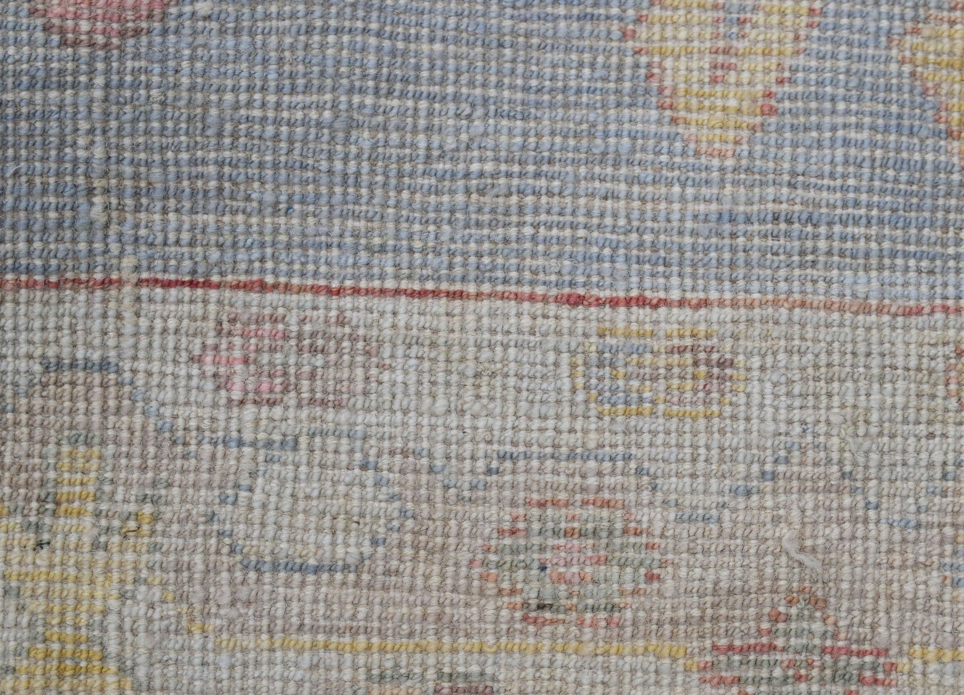 A close-up of a handwoven wool runner featuring a transitional floral pattern in muted tones.