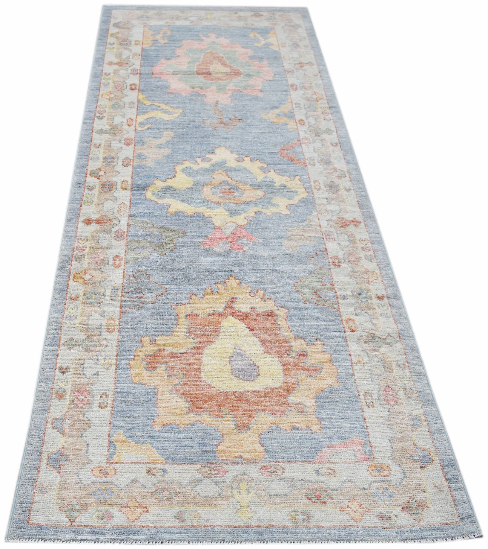A handwoven wool runner rug featuring a transitional Oushak floral pattern in blue and soft tones.