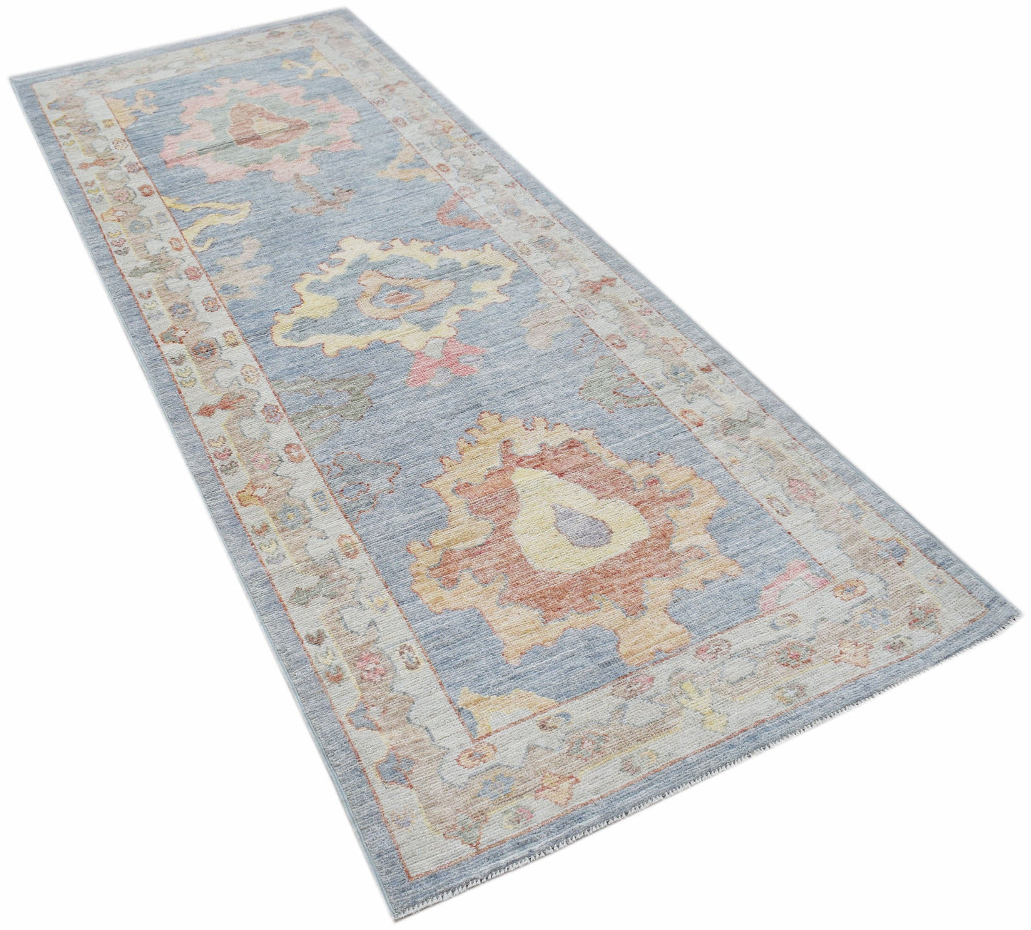 A handwoven wool runner rug featuring a transitional floral pattern in blue and muted earth tones.