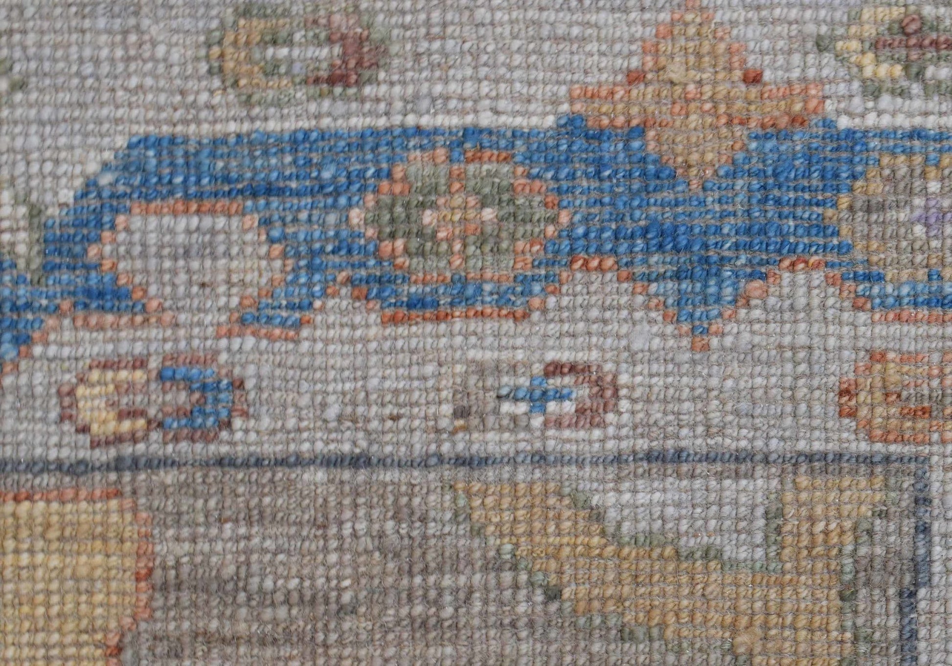 A close-up view of a handwoven wool rug featuring a transitional floral pattern in blue and tan.