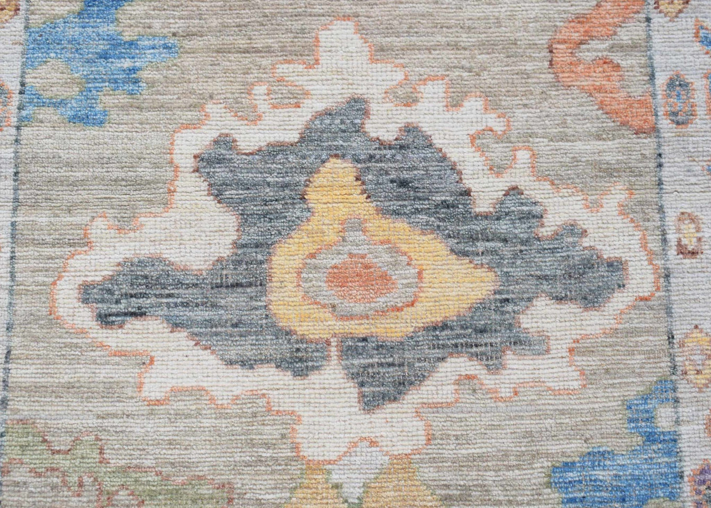 A handwoven wool runner rug featuring a transitional floral pattern in blue, orange, and grey.