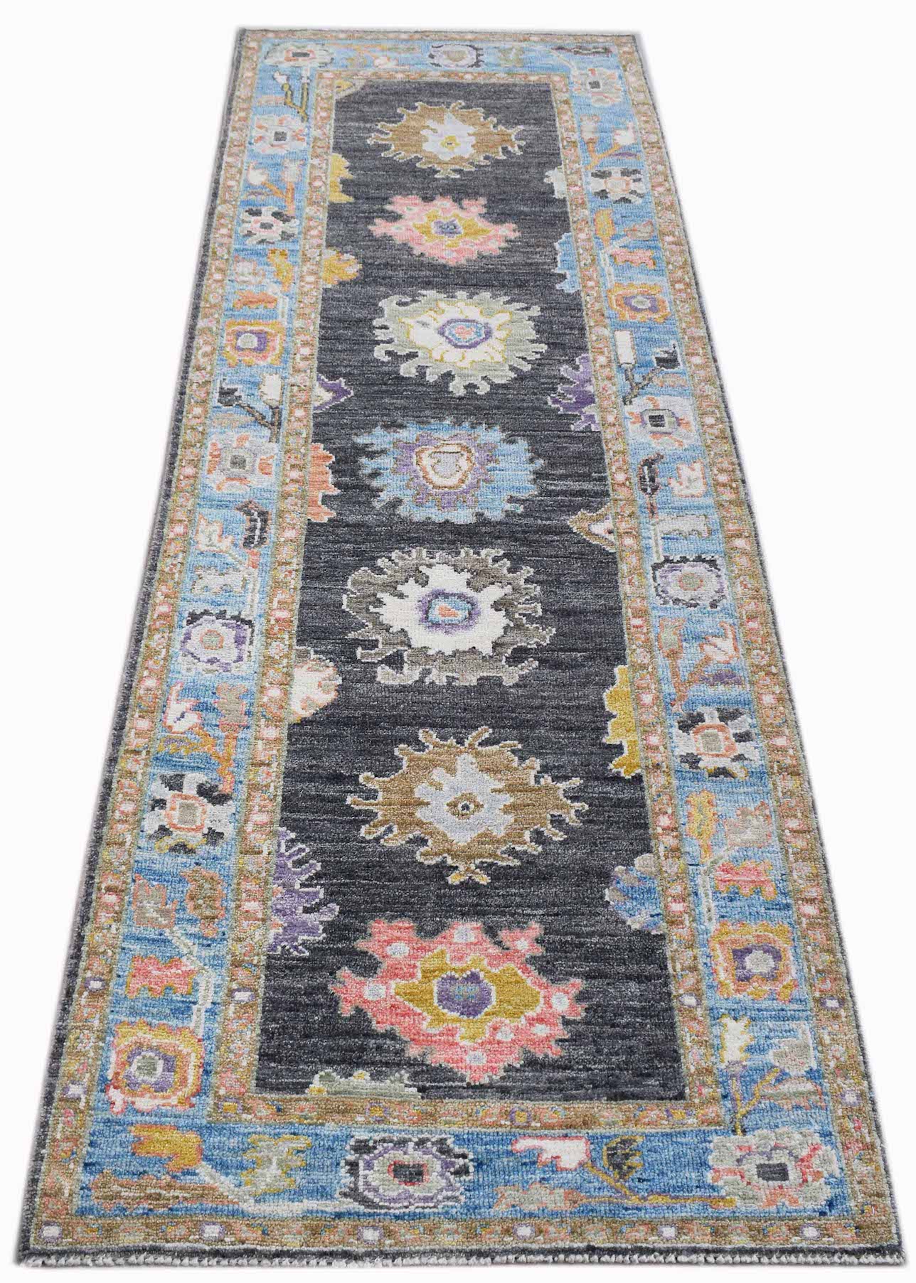 A handwoven wool runner rug featuring a dark grey field with colorful floral Oushak motifs.