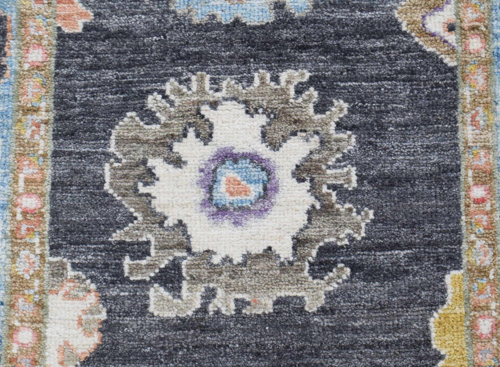 A handwoven wool runner featuring a floral medallion pattern in muted tones on a dark grey field.