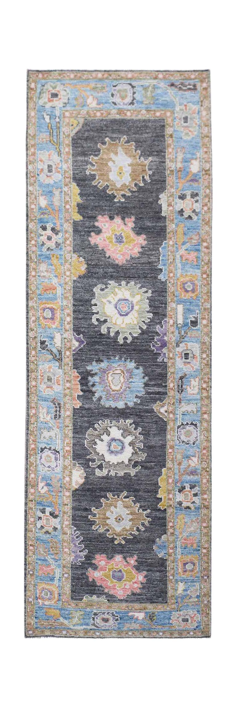 A handwoven wool runner rug featuring a dark grey field with colorful floral medallions.