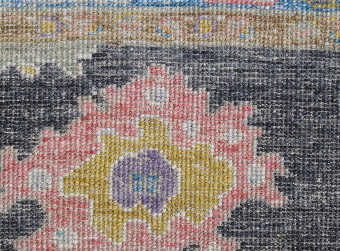 A close-up of a handwoven wool runner featuring a floral pattern in pink, yellow, and purple.