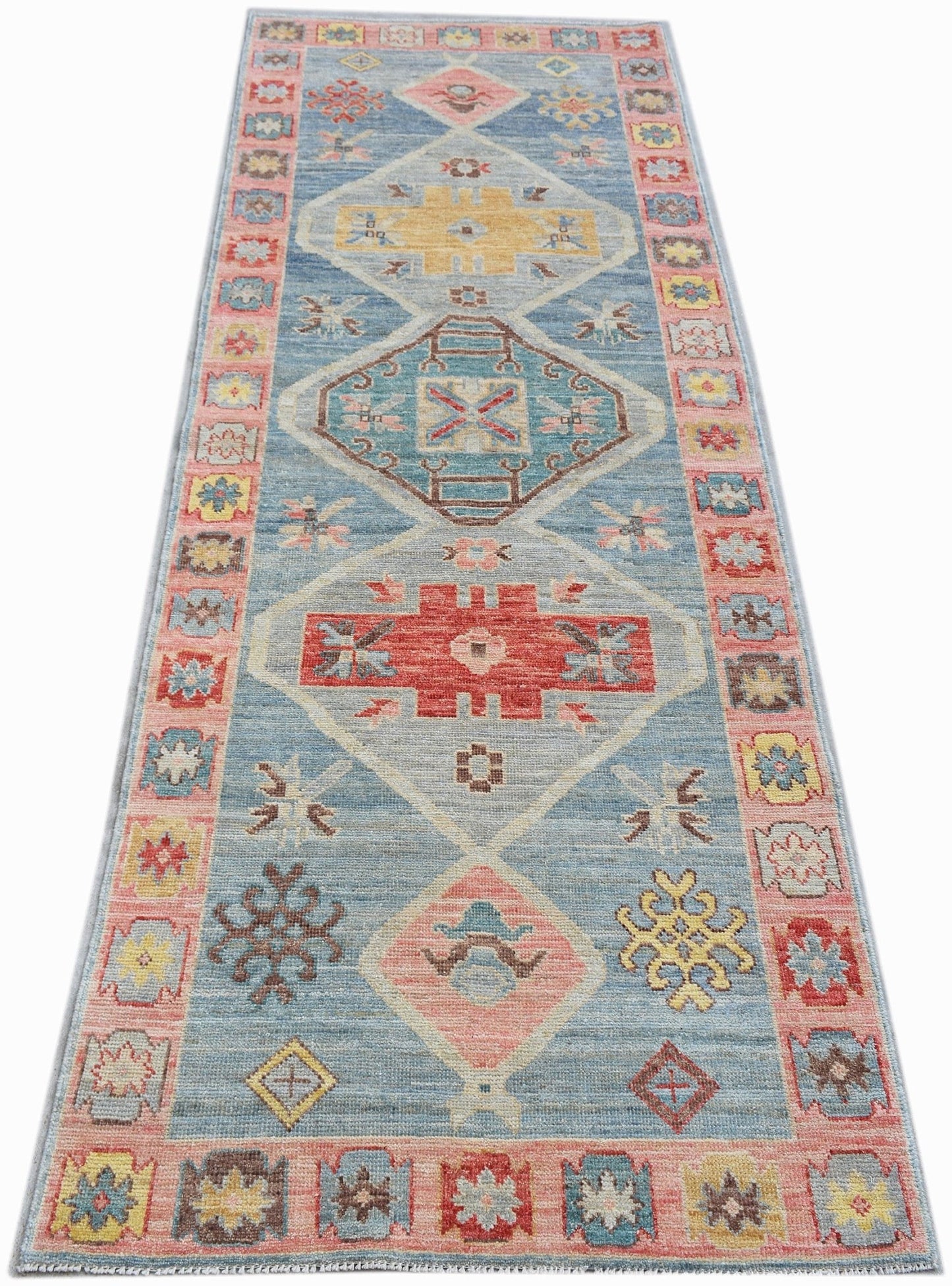 A handwoven transitional Oushak runner rug featuring geometric patterns in blue, pink, and yellow.